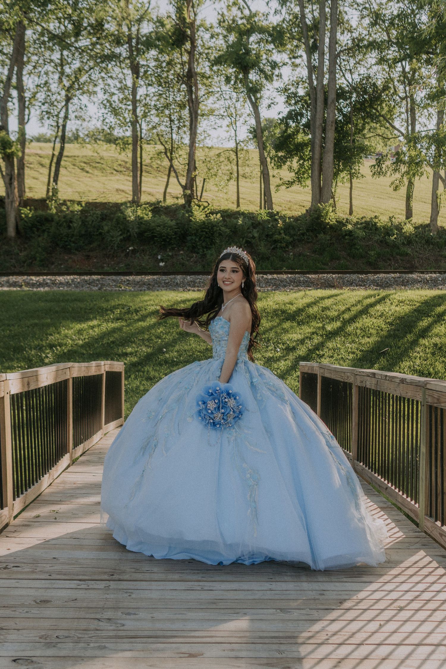 A stunning quinceañera photo session on a wooden bridge featuring a flowing light blue ballgown dress.