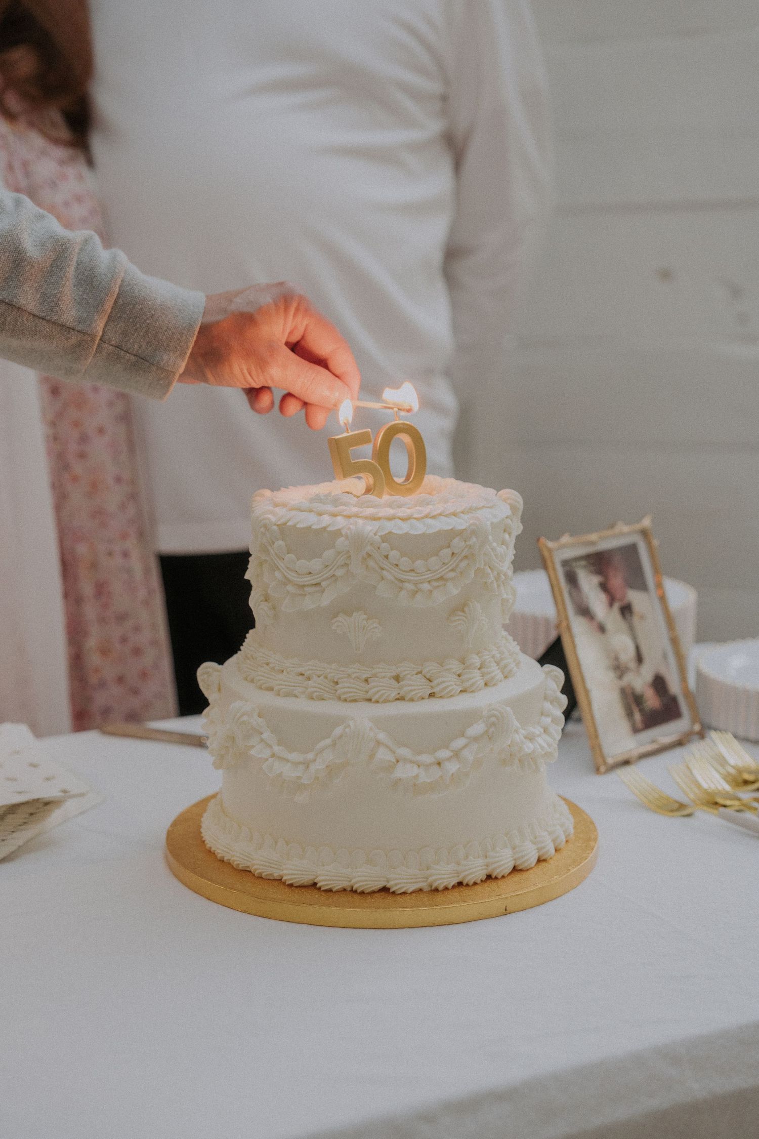 White frosted anniversary cake with gold number 50 topper being decorated on a table.