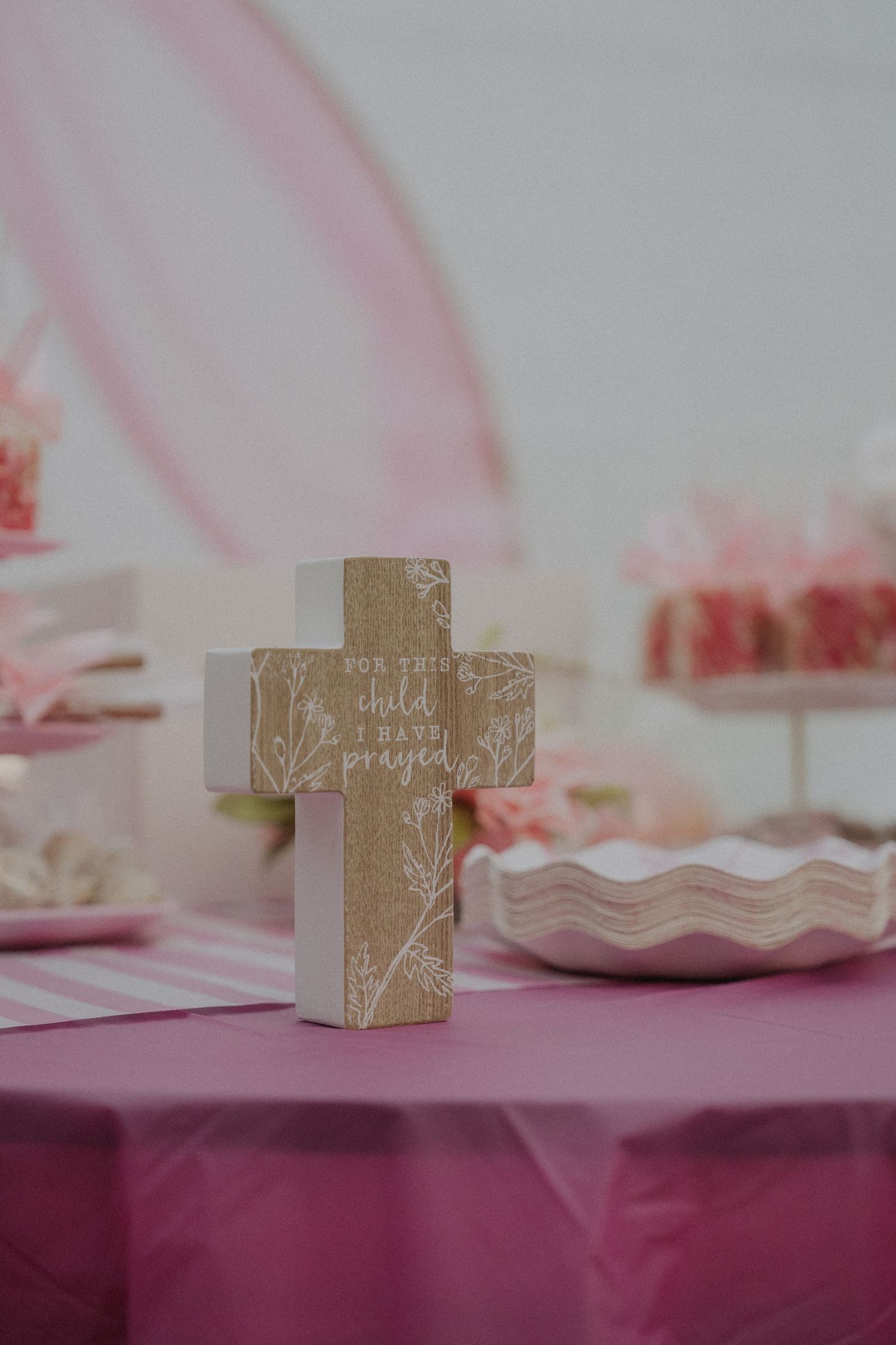 Decorative gold cross displayed on a pink table setting for a religious celebration.