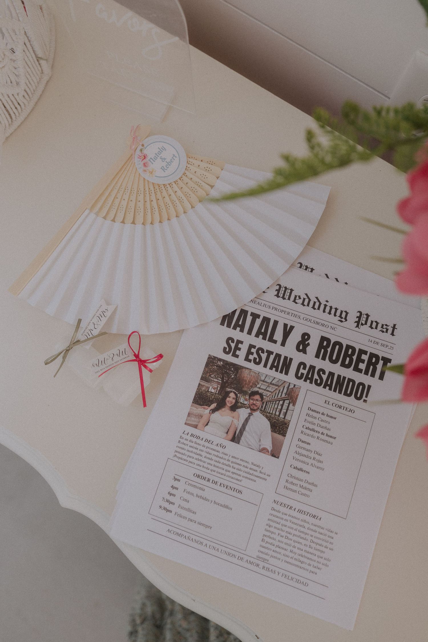 Wedding newspaper program for Nataly and Robert beside decorative paper fans on a table.