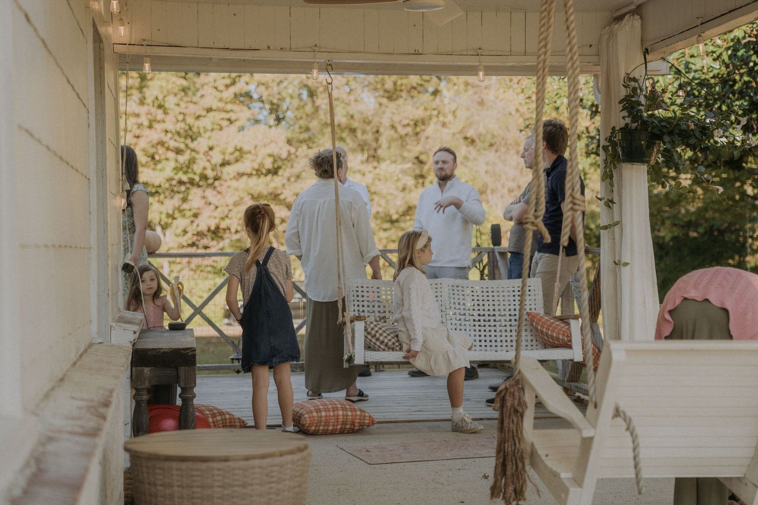 Rustic covered porch decorated for a celebration with guests mingling in natural light.