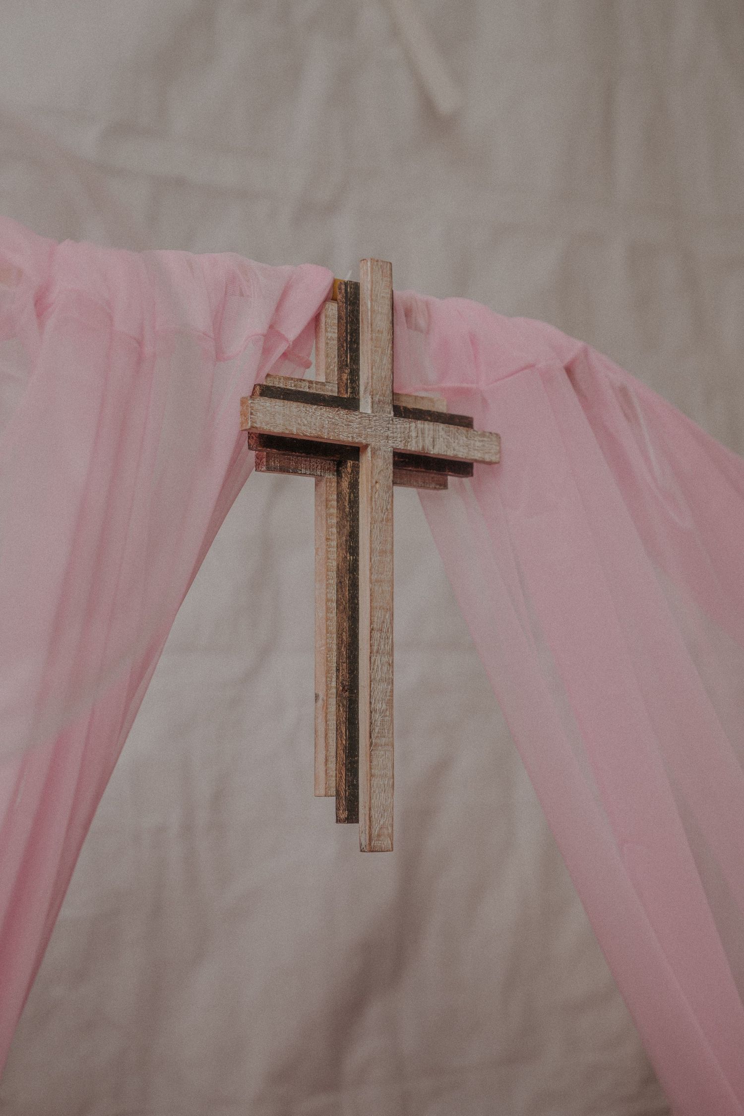Wooden cross decoration against pink tulle fabric backdrop.