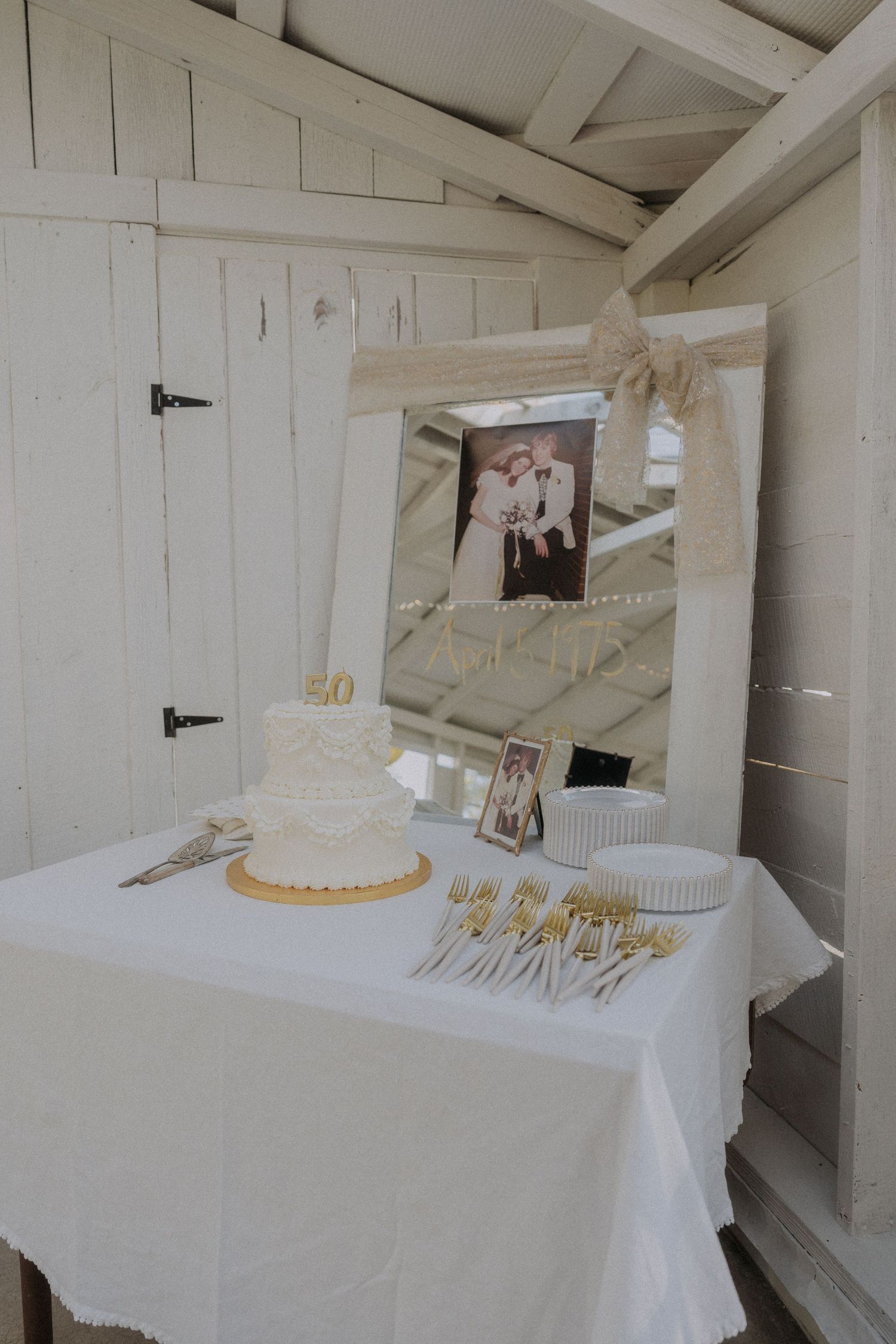 White wedding cake and decorations displayed on a table against white paneled walls.