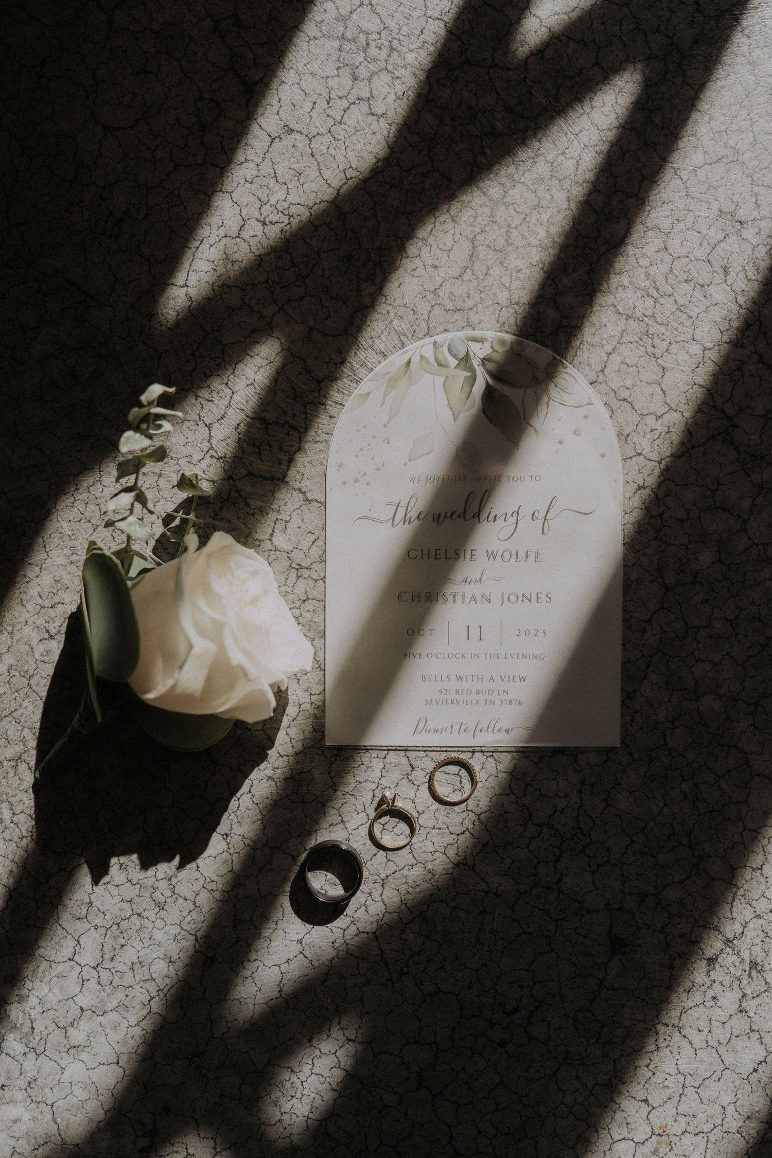 Artistic color wedding details with dramatic shadows showing invitations, rings and flowers on textured surface.