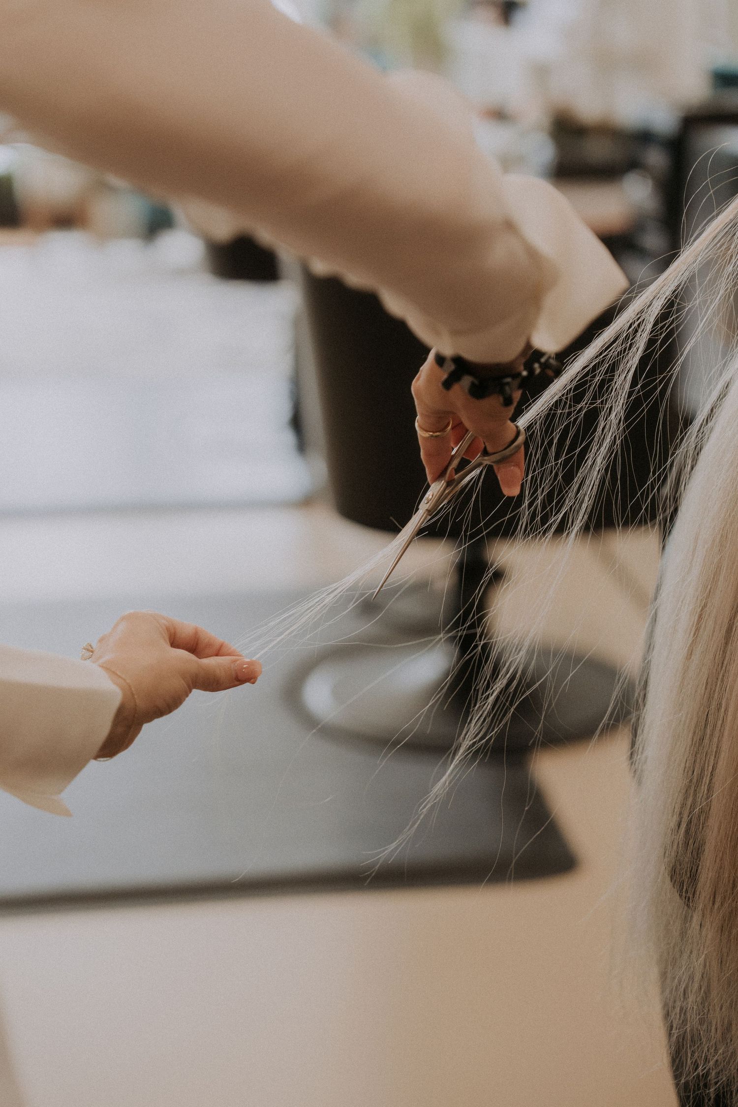 Close-up of hands styling long blonde hair in a professional salon setting.