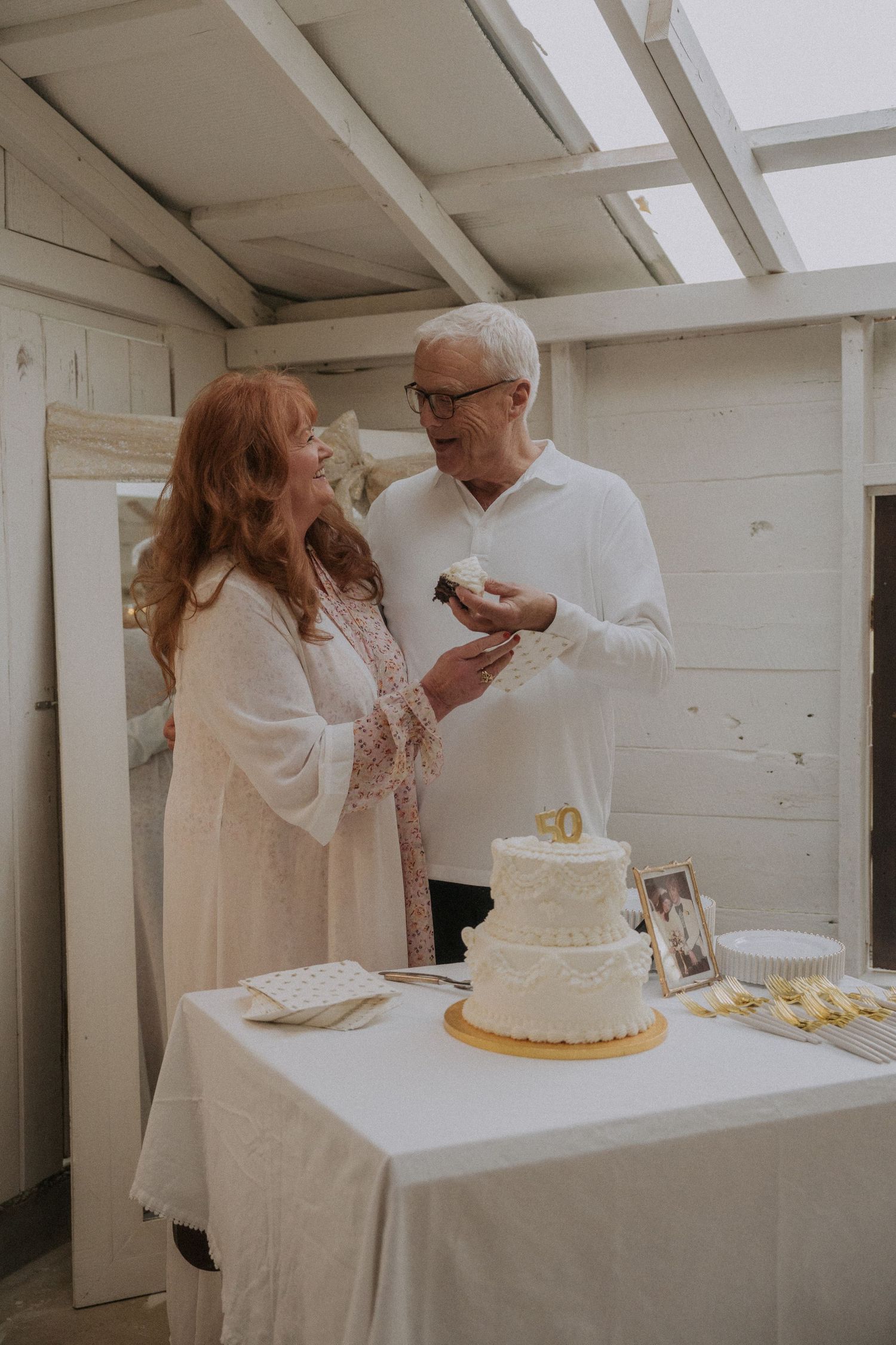 A couple sharing a sweet moment while cutting their anniversary cake in a white indoor setting.