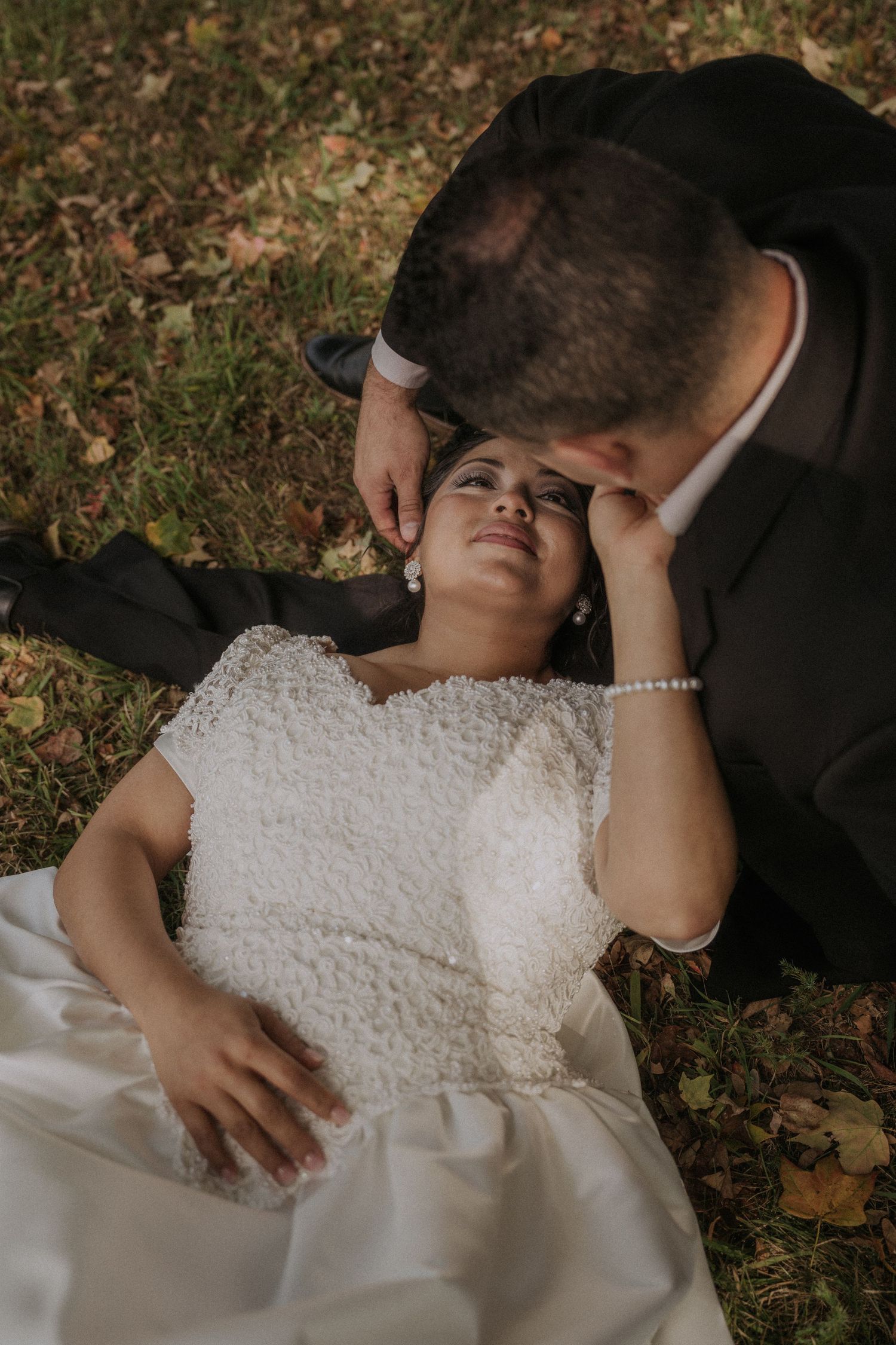 Romantic wedding couple poses lying on grass during outdoor photoshoot.