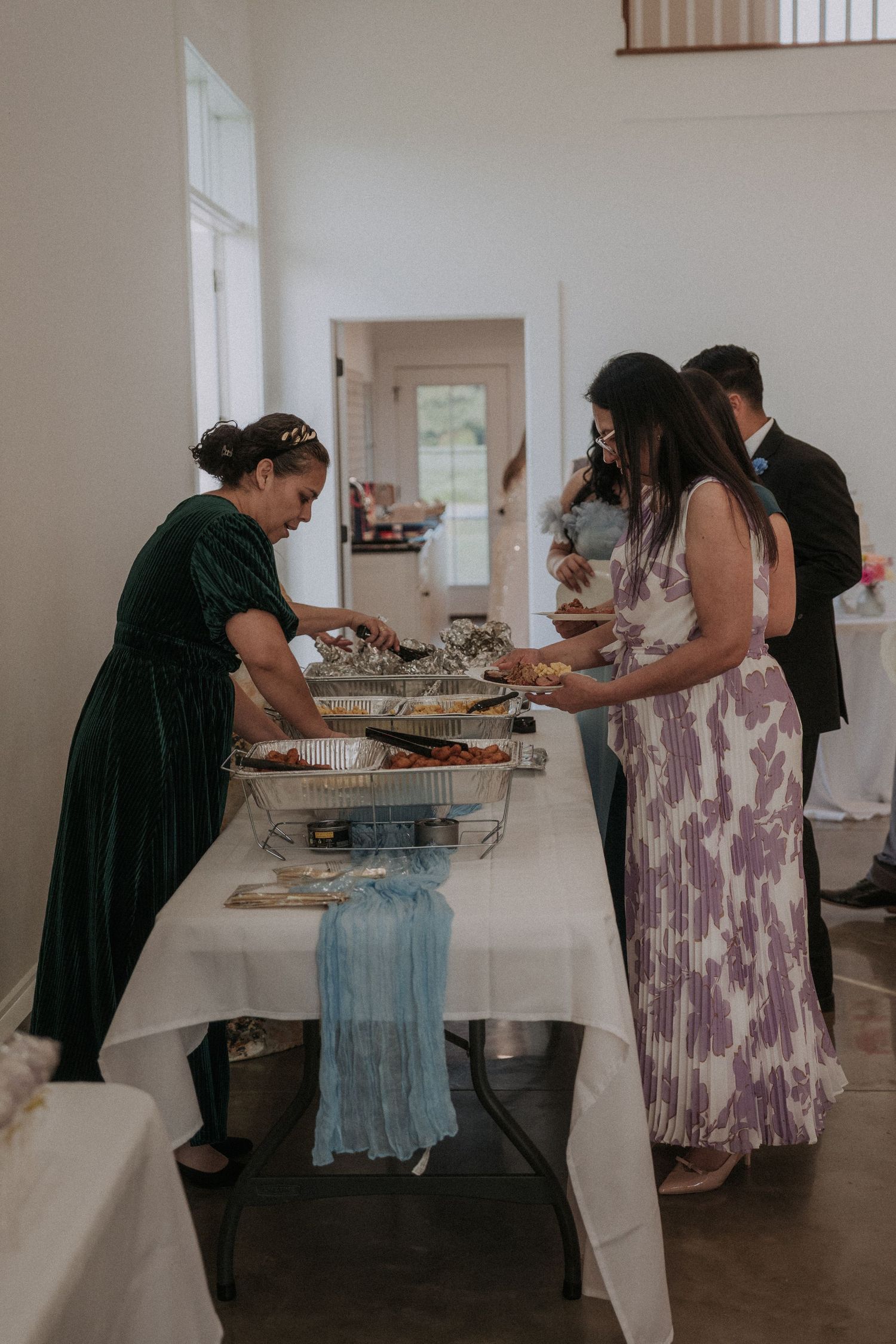 Guests serving themselves at a buffet table with chafing dishes at an elegant indoor wedding reception.