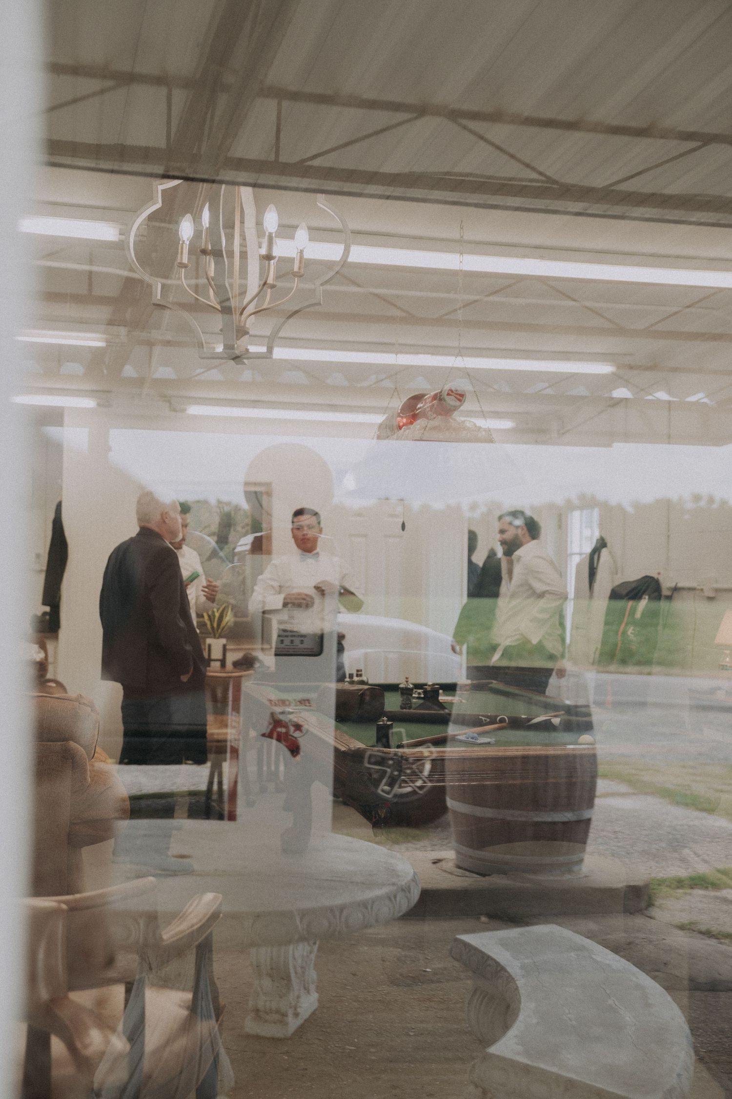 Guests mingle at an elegant outdoor wedding reception venue viewed through a glass window reflection.