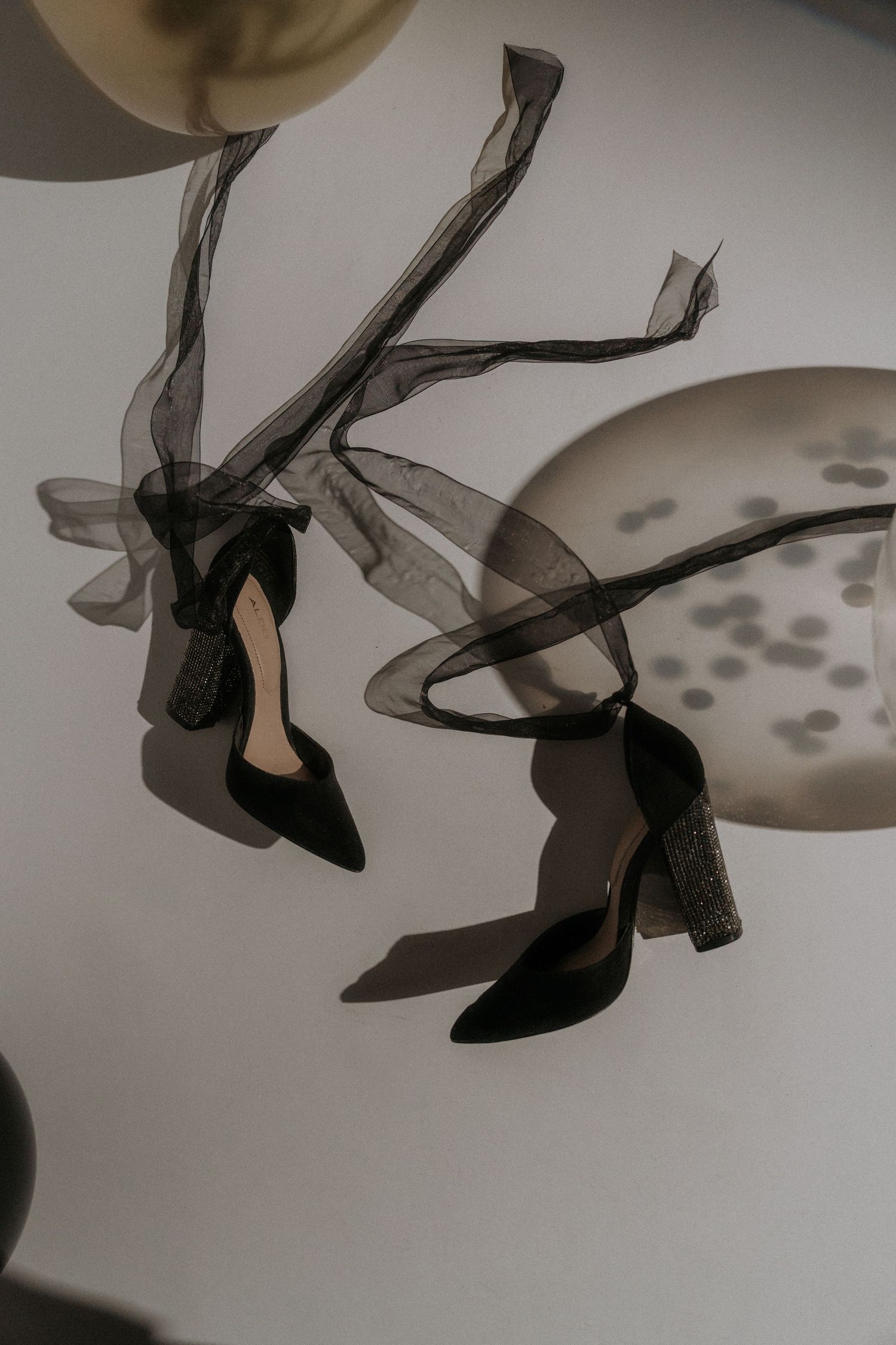 Abstract composition of flowing black fabric, heels, and shadows on white background.