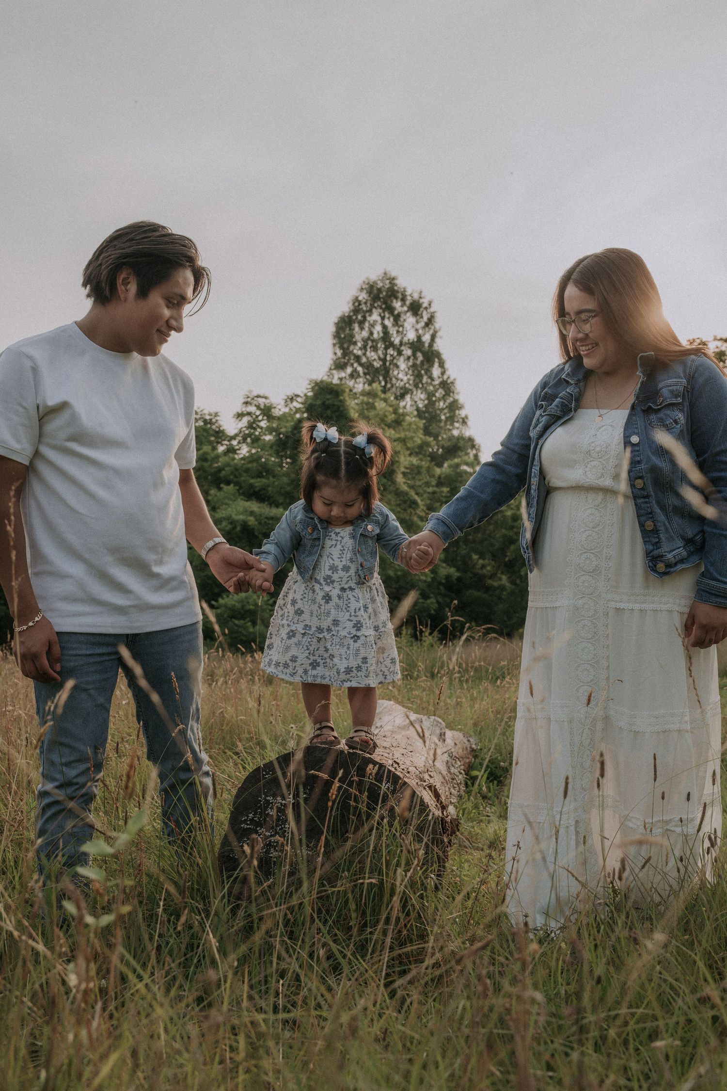Family walking together through tall grass in a rustic outdoor field at sunset.