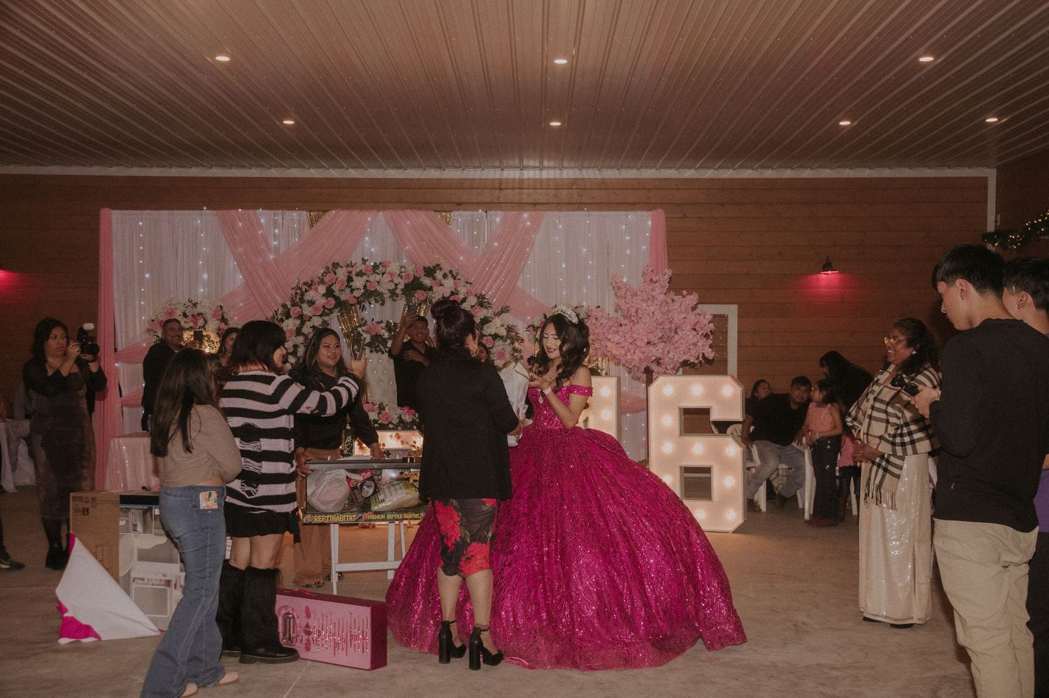 Party guests mingle in a wood-paneled venue decorated with pink and white accents.