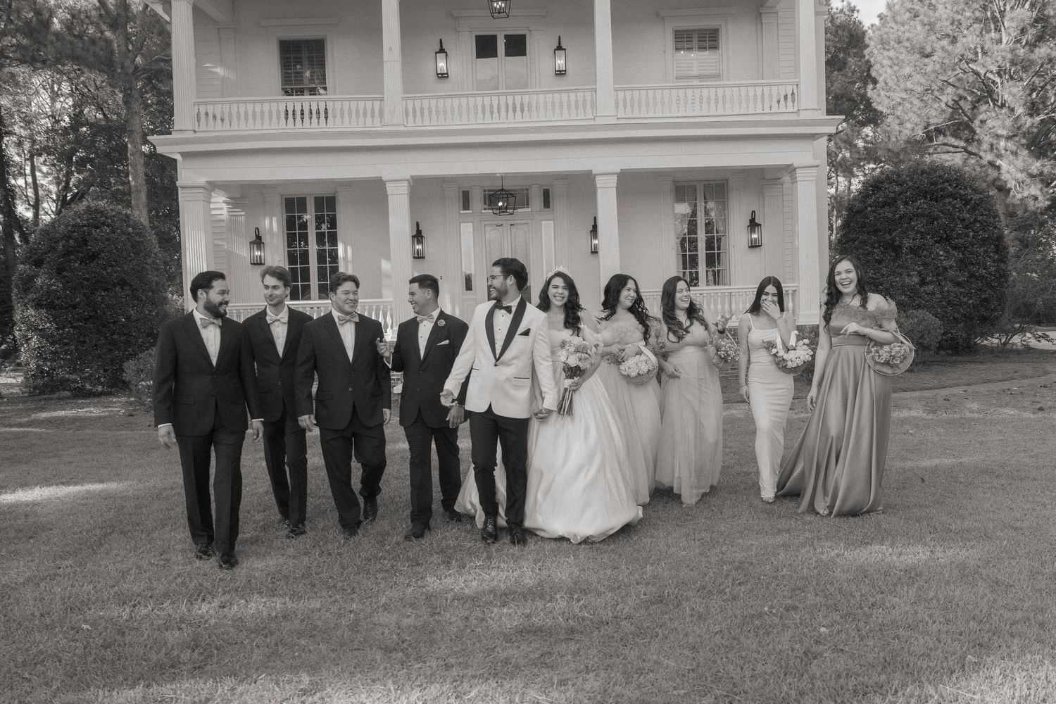 Black and white wedding party walking in front of elegant white mansion with groomsmen and bridesmaids.