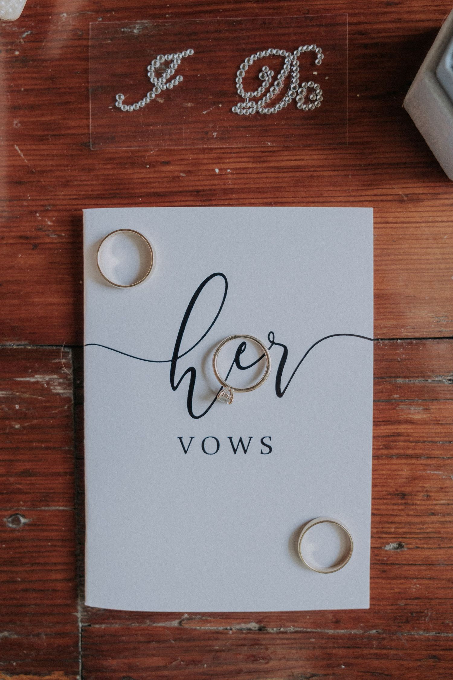 Her vows booklet with gold wedding rings on rustic wood table.