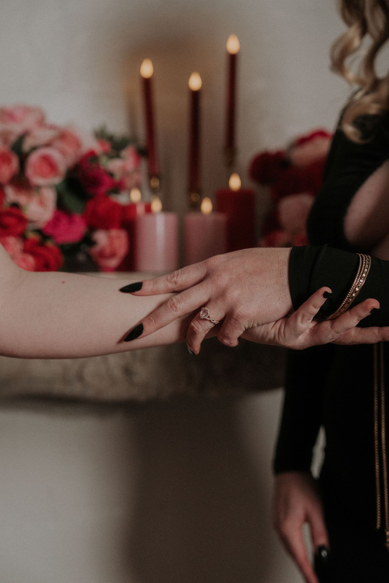 Close-up of hands with lit candles and pink roses in the background.