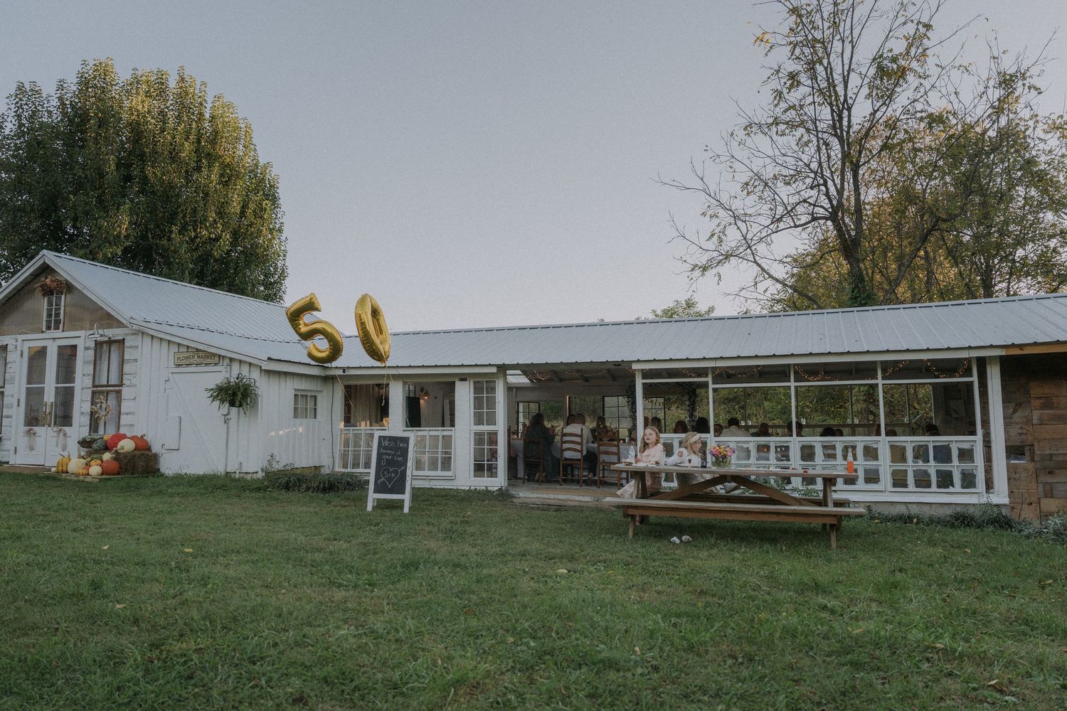 Long white ranch house with metal roof viewed from across a grassy field.