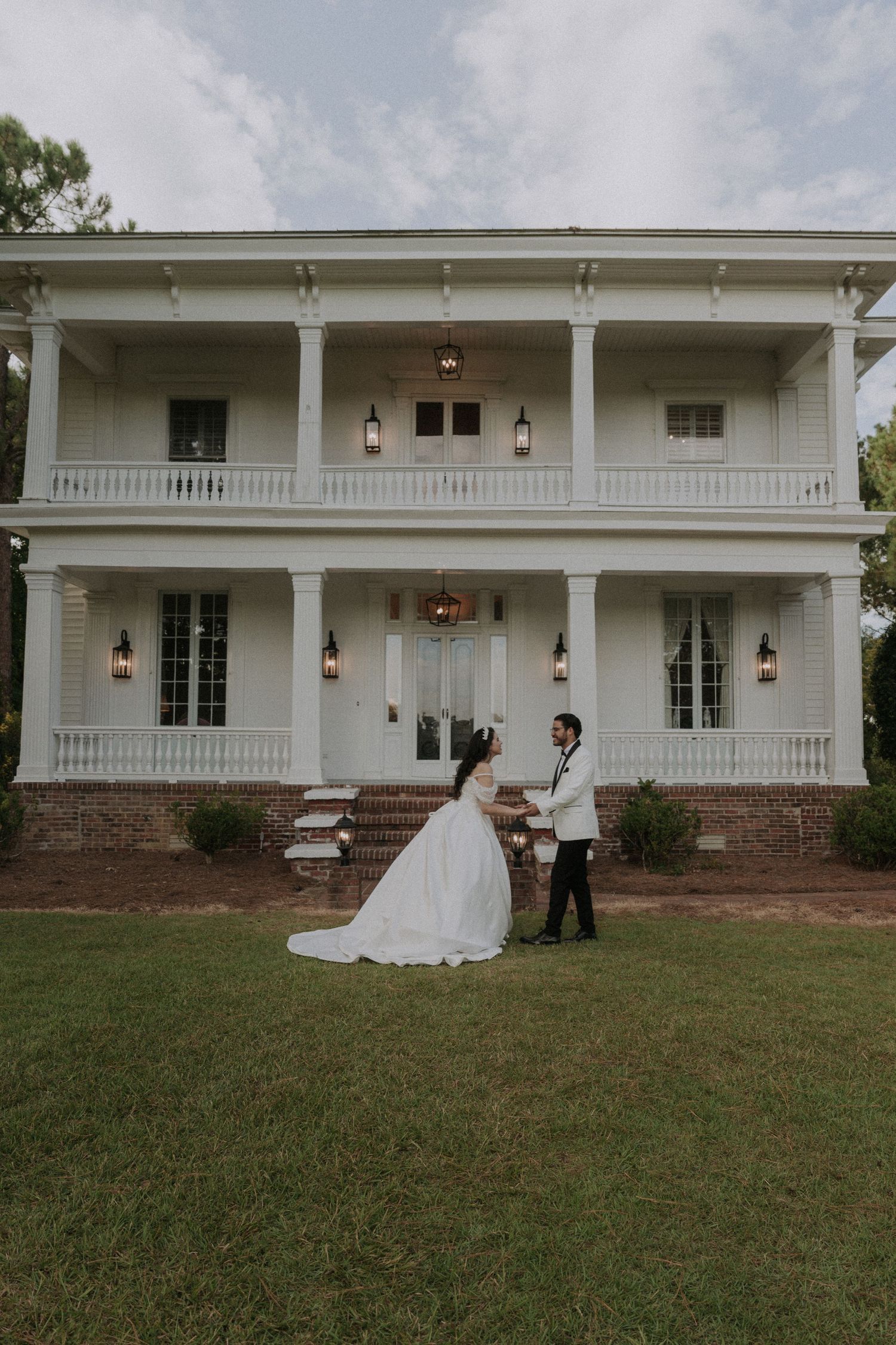 Bride and groom share a romantic moment on the lawn of a grand white Southern plantation wedding venue.