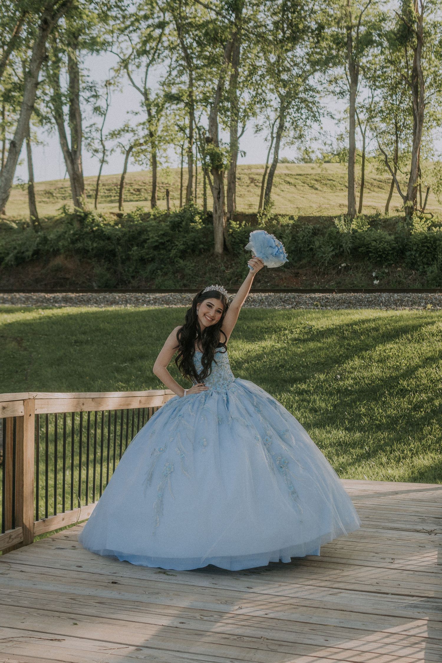 Elegant blue princess gown photographed for a quinceañera on an outdoor wooden platform.