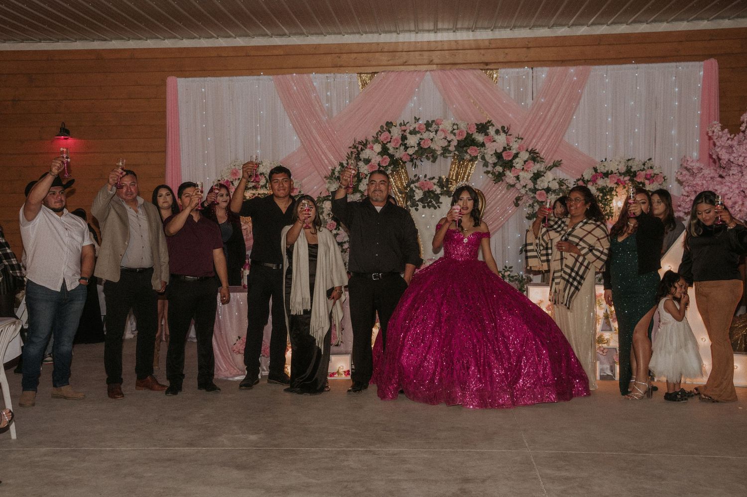 Guests gather at a Sweet 16 celebration with pink decor and floral arrangements for a toast.