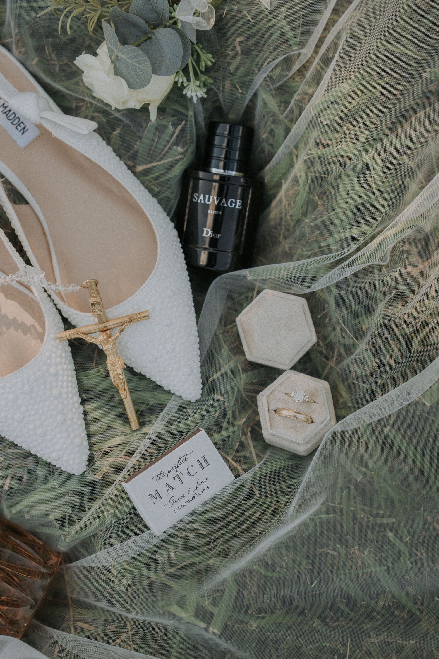 Bridal accessories including white pointed shoes and perfume bottle arranged on delicate fabric.