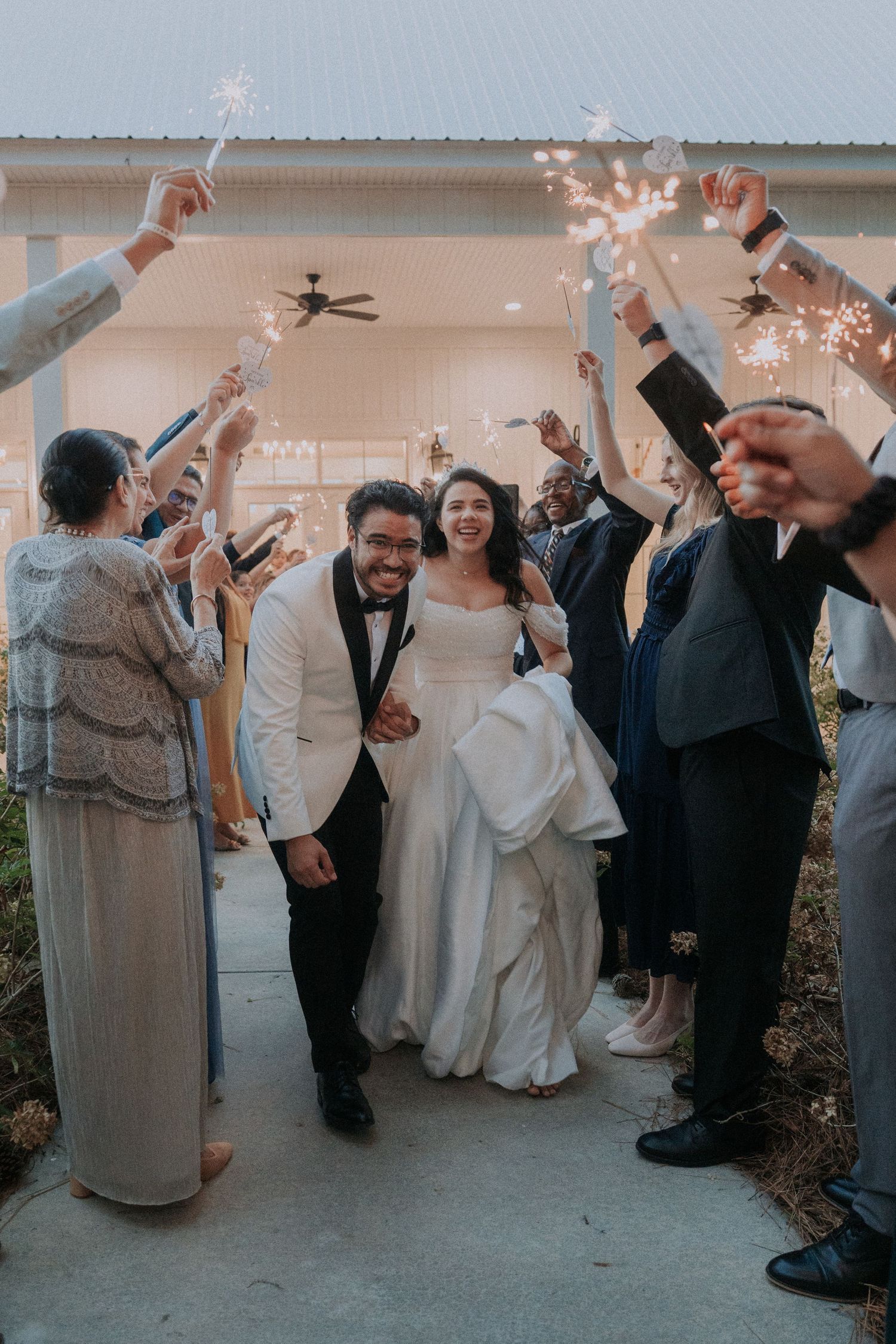 Newlywed couple walks through sparkler tunnel surrounded by cheering guests during romantic wedding send-off celebration.