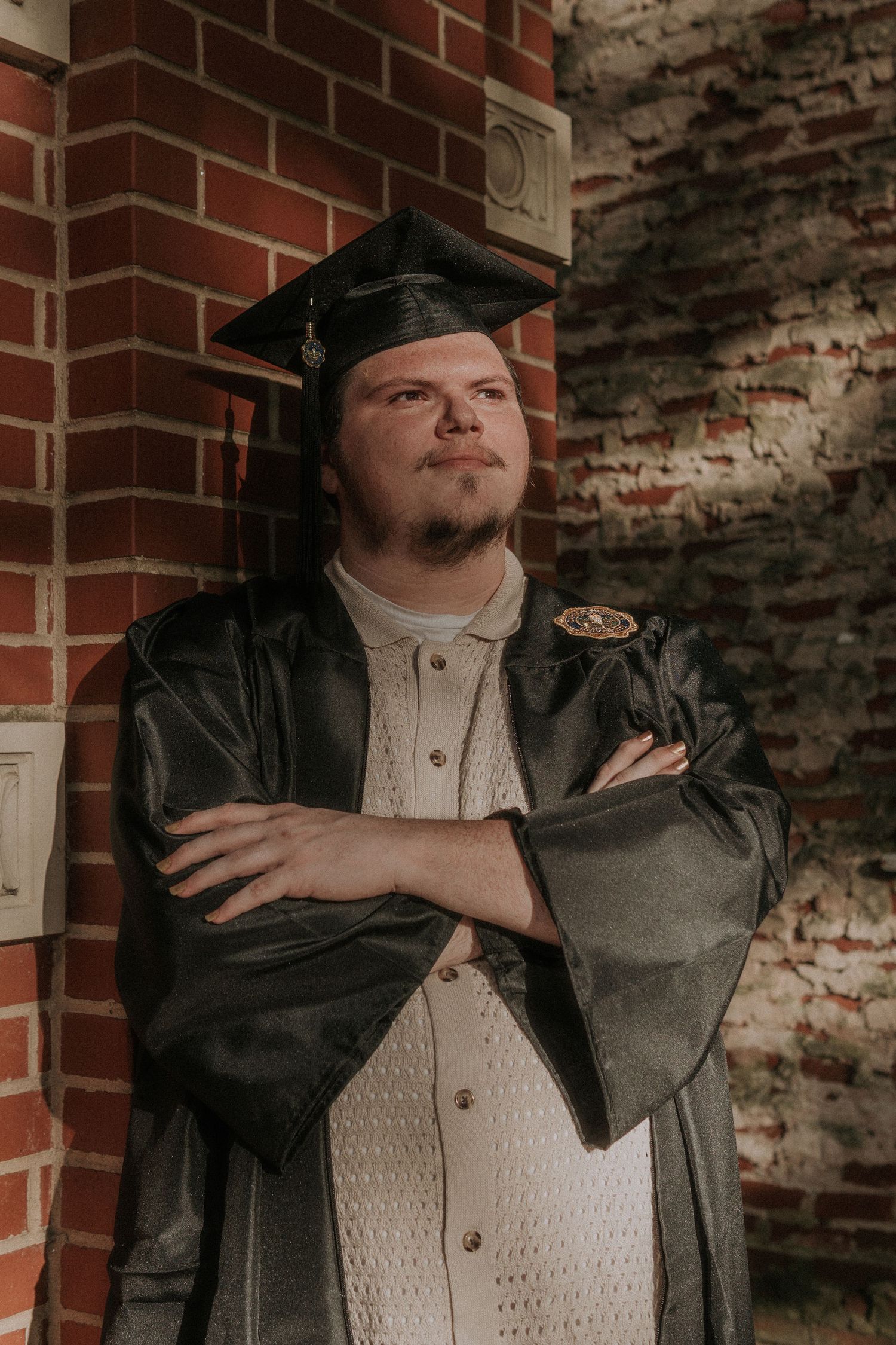 Male graduate posing against brick wall wearing graduation cap and gown