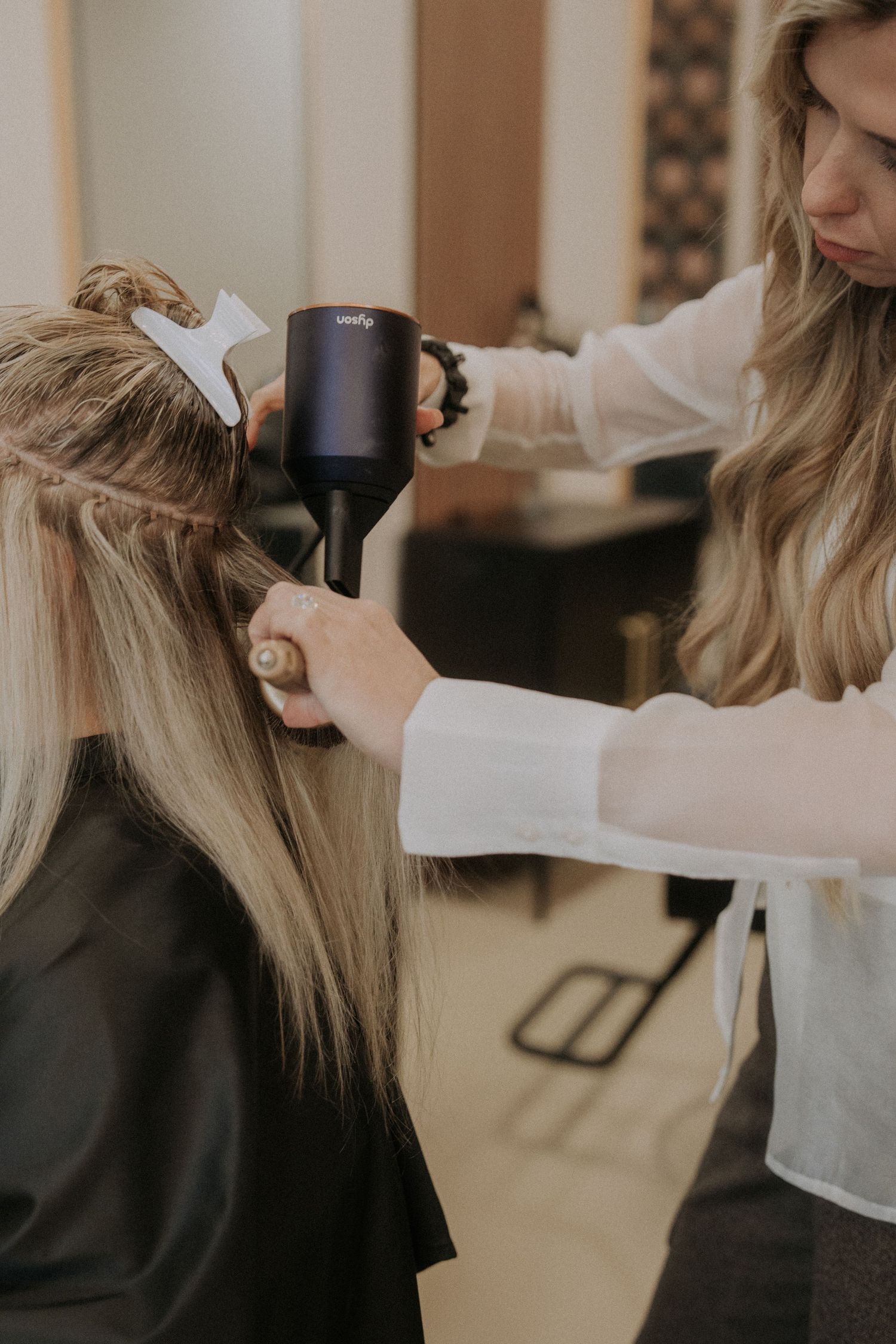 Hair extension session in progress showing detailed work with professional tools.