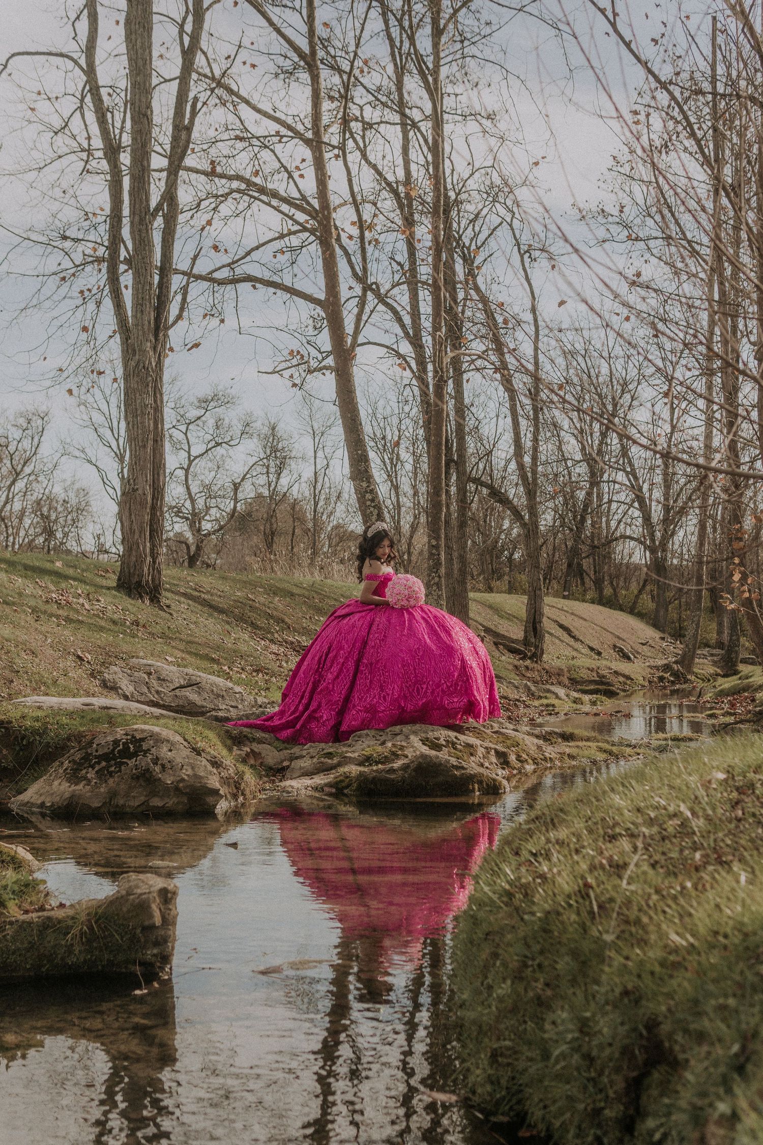 Magenta ballgown reflected in a serene creek surrounded by bare winter trees.