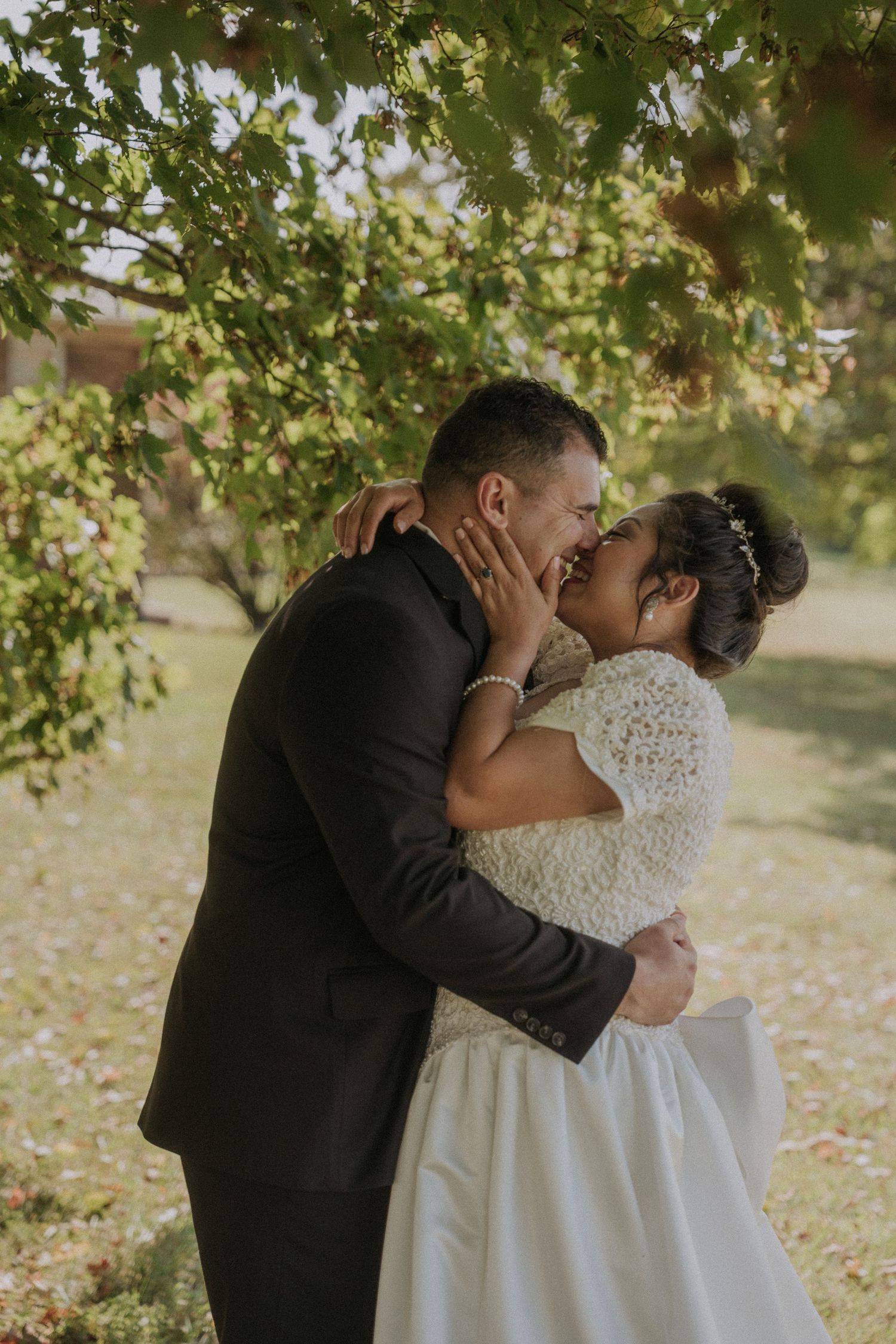 Romantic wedding couple sharing intimate moment under tree canopy.