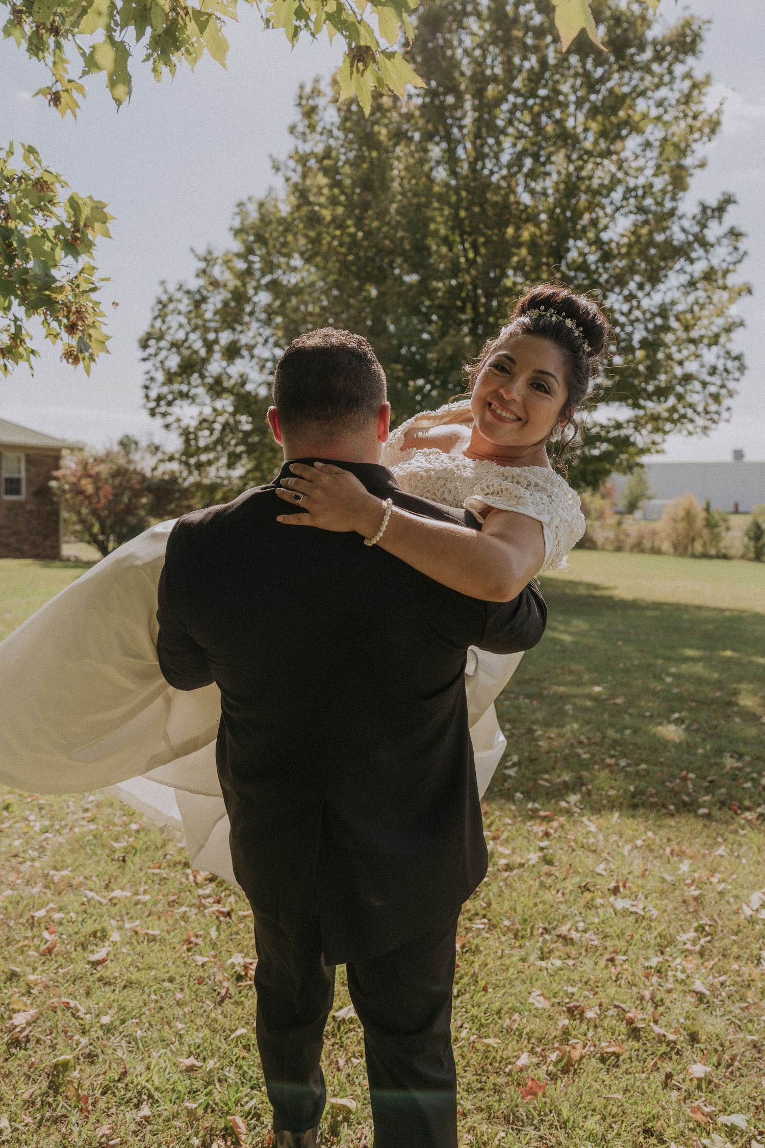 Playful wedding couple dancing and spinning on grassy hillside.