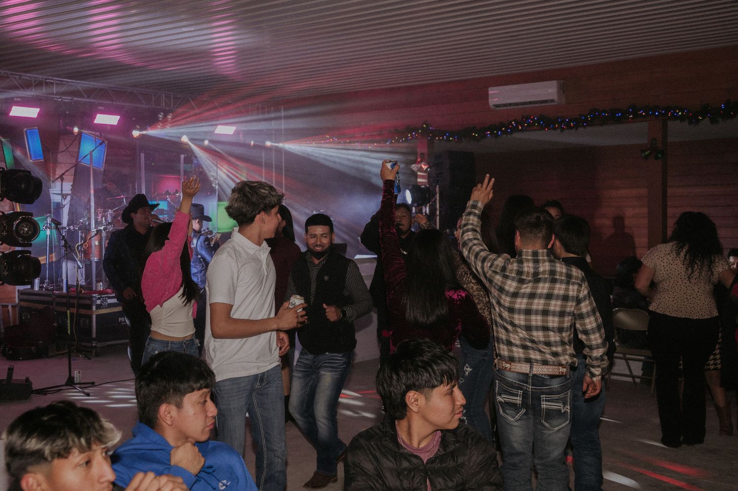 Dark indoor venue with colorful lighting and people gathering for a Sweet 16 party.