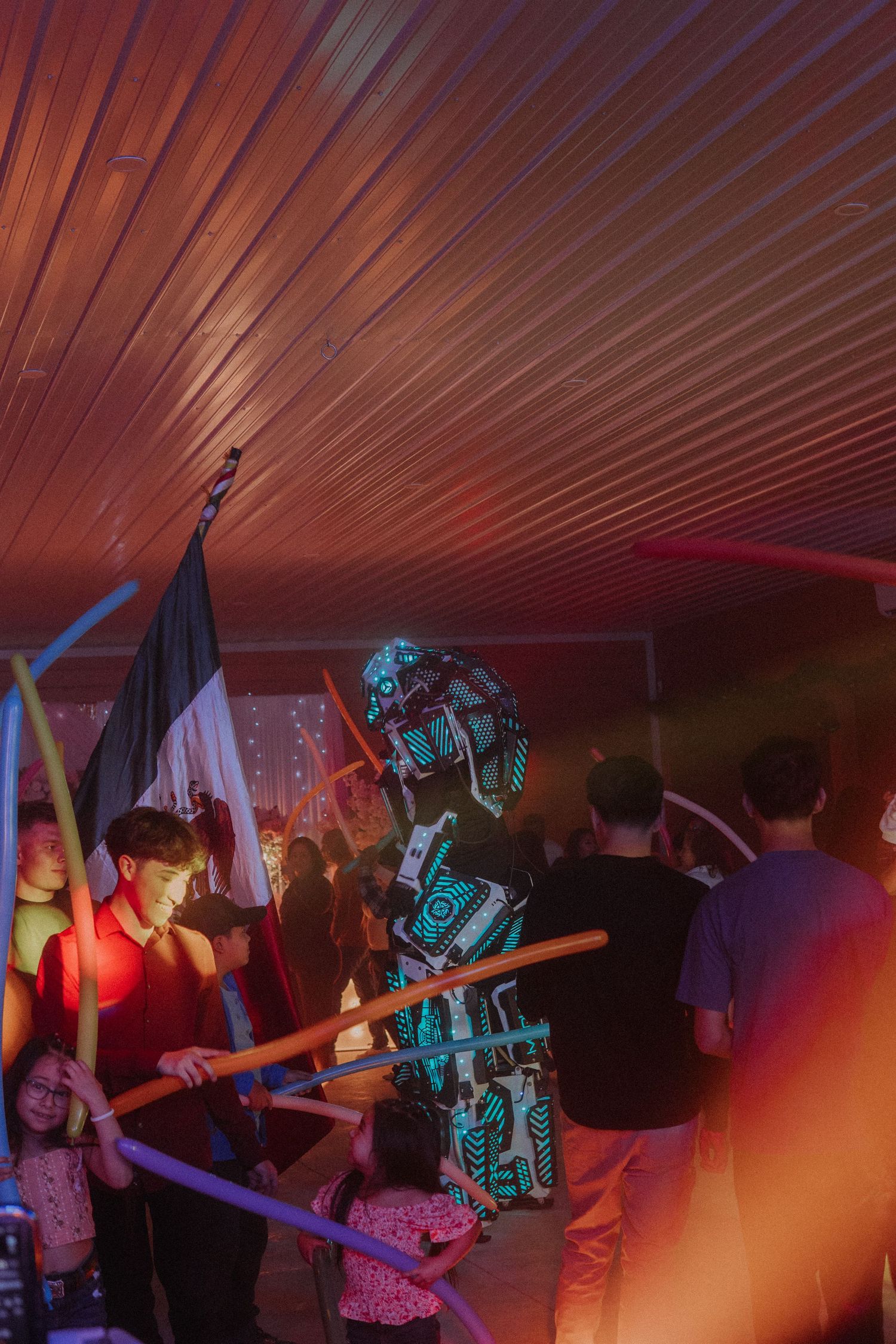 Glowing robot costume performs among dancing party guests under colorful lights at a Sweet 16 party