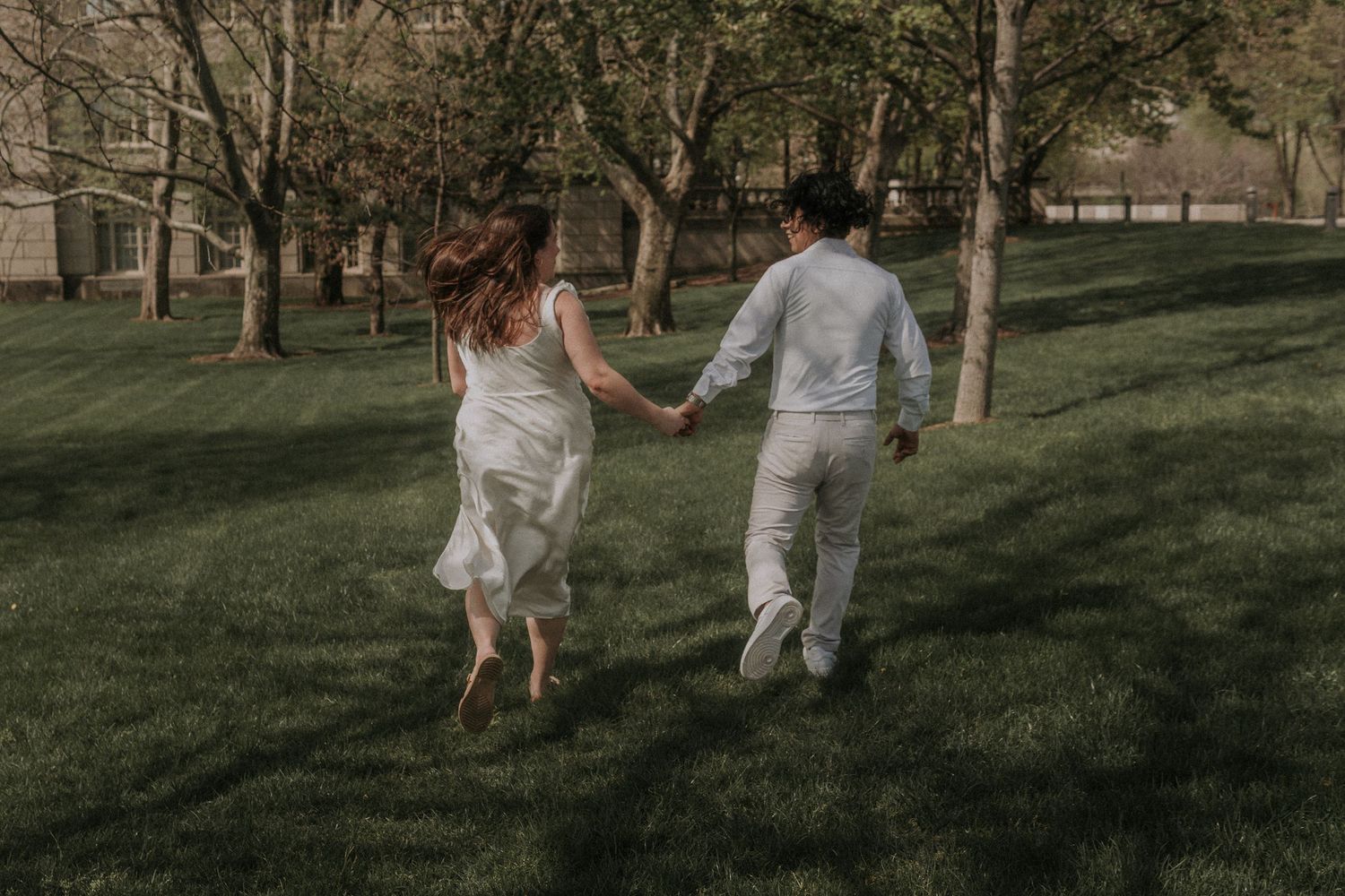 Two people running together on grass path through park with trees.