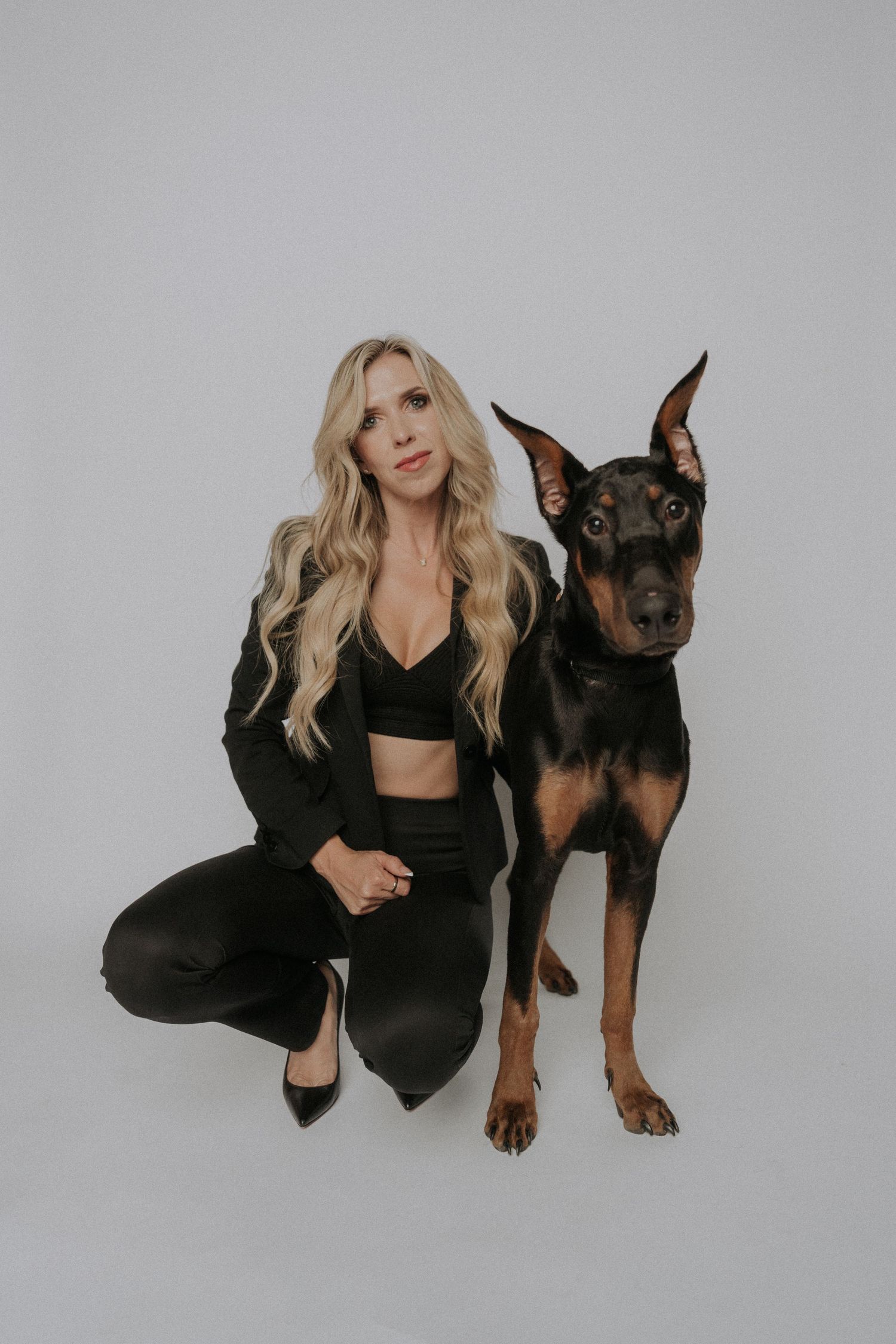 A woman in black poses with a large Doberman dog against a white studio background.