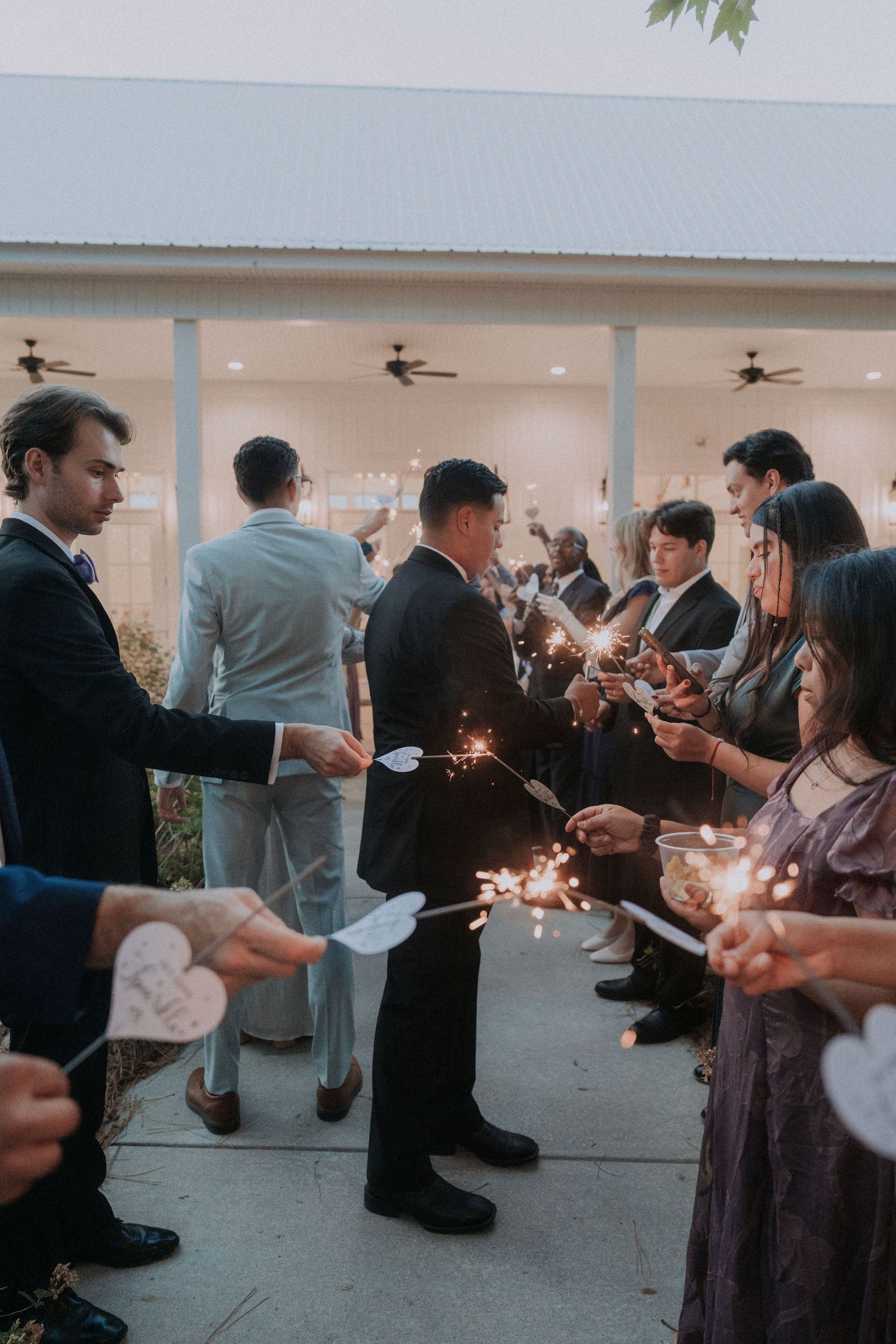 Wedding guests holding sparklers to create a romantic send-off tunnel for the newlyweds outside a venue.
