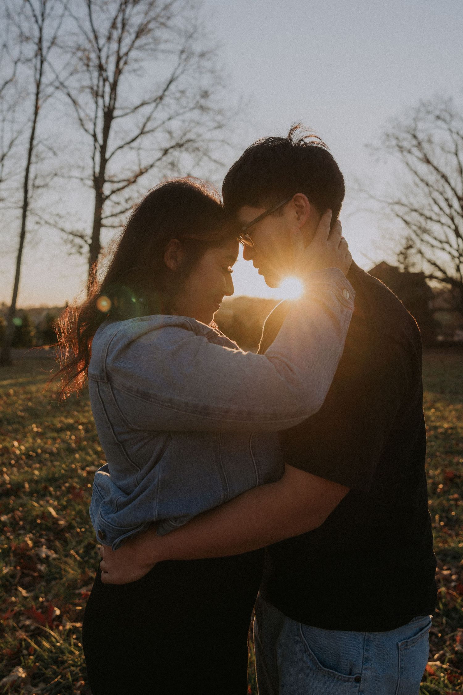 A couple embraces in silhouette against a dramatic sunset through bare winter trees.