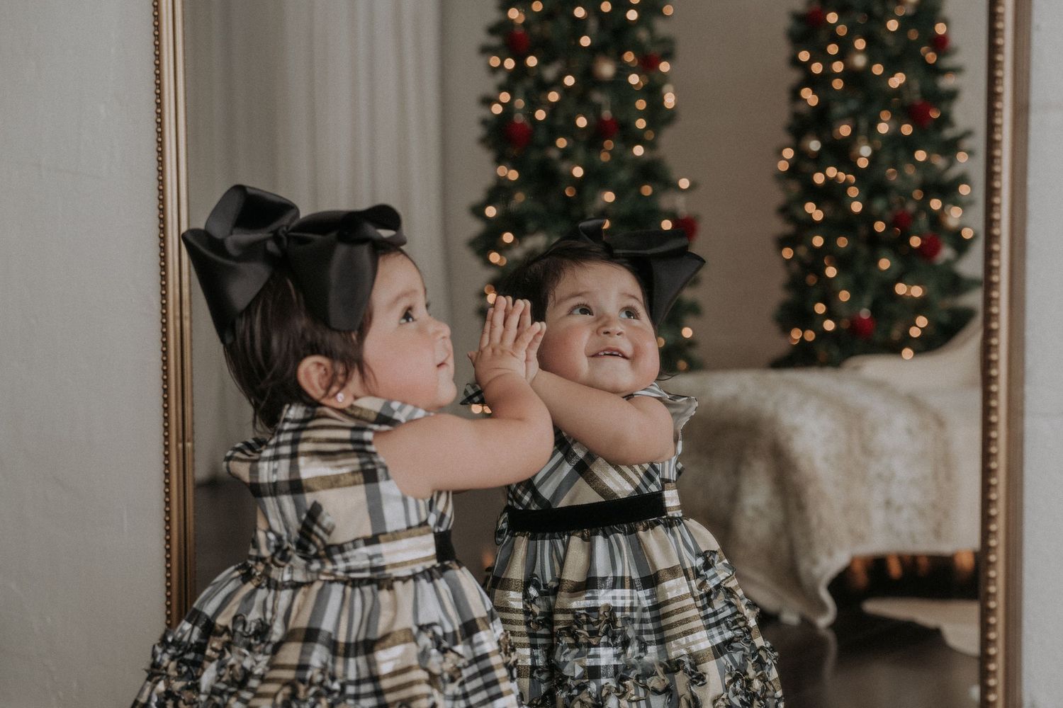 A child poses playfully in front of decorated Christmas trees with twinkling lights.