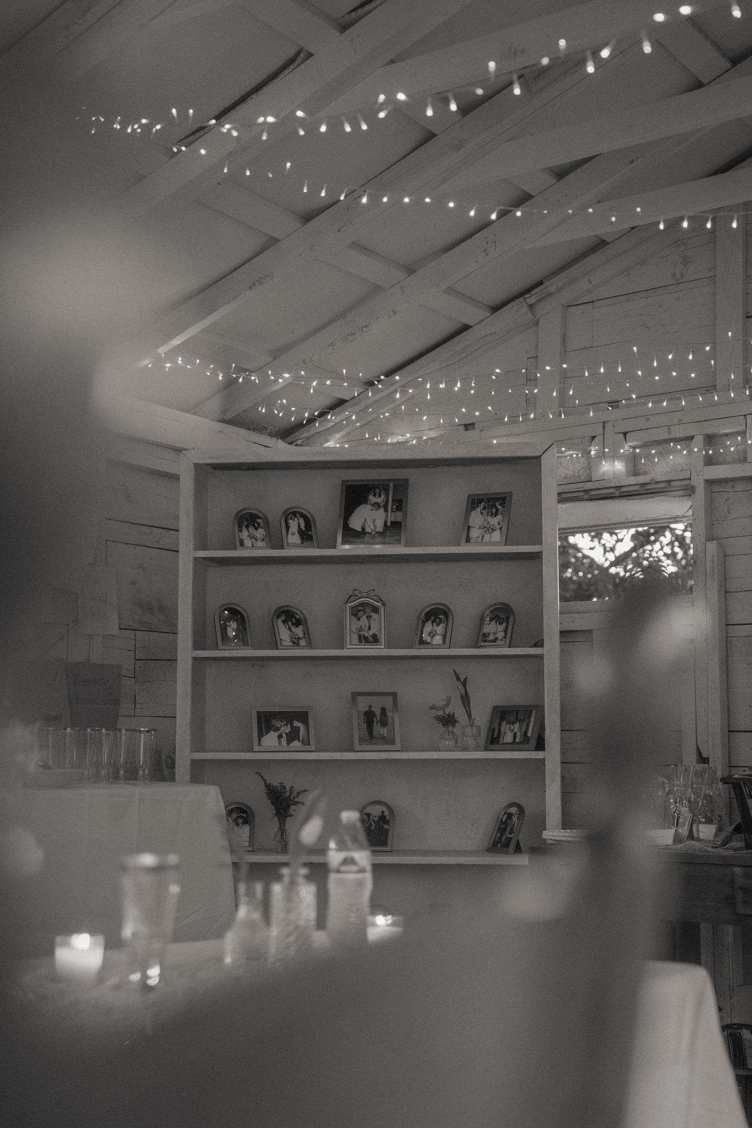Black and white photo of indoor venue with string lights and photo display shelves creating romantic ambiance.