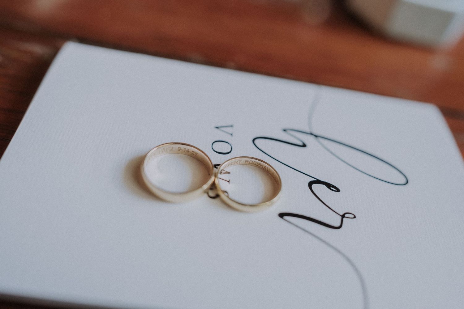 Two gold wedding bands resting on a white card with elegant script lettering for a wedding ceremony.