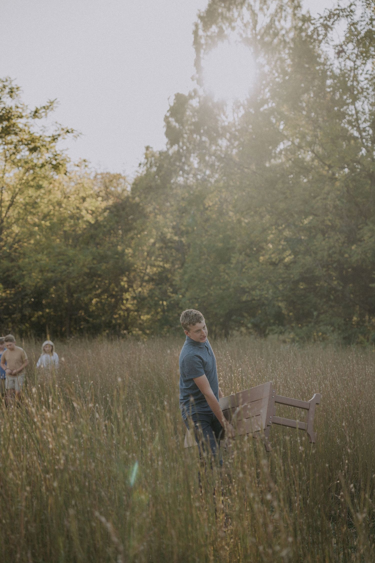 People walking through a tall grass field during golden hour with trees in the background.