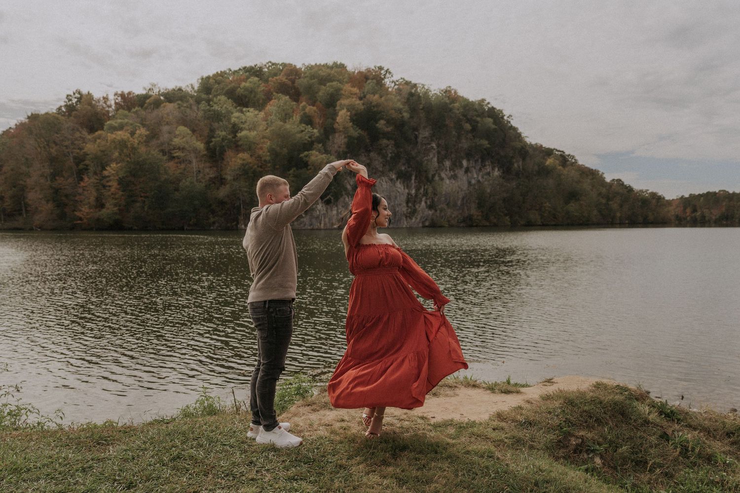 Two people dance together in flowing outfits by a scenic lake during golden hour.