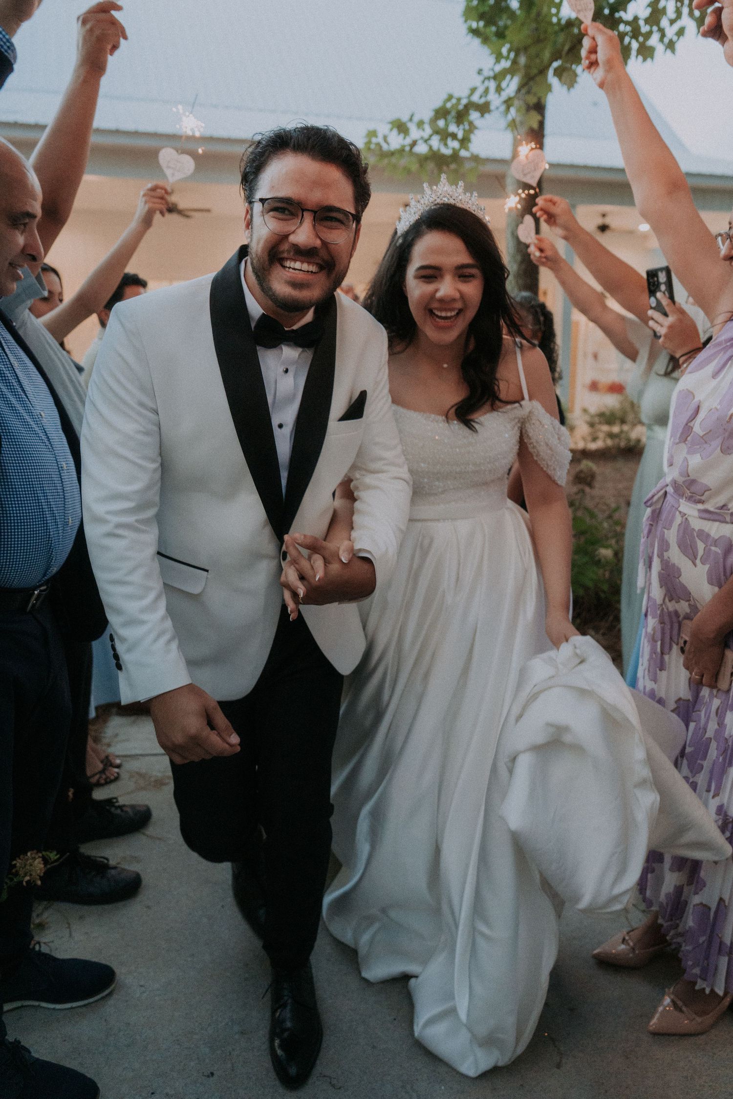 Joyful newlyweds in wedding attire walk through a sparkler exit, smiling as guests celebrate around them.