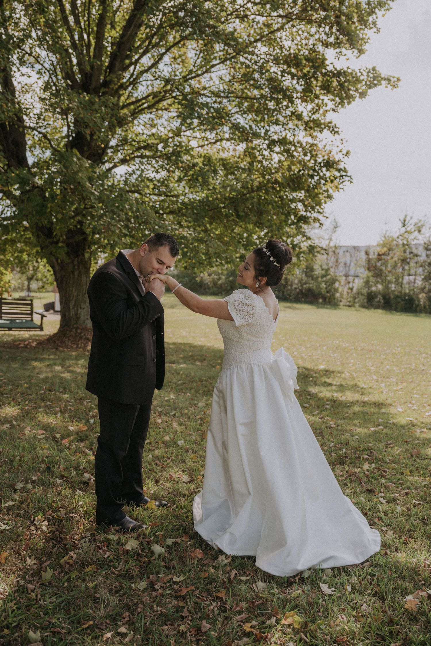 Wedding couple dancing and twirling in a grassy outdoor setting with trees.