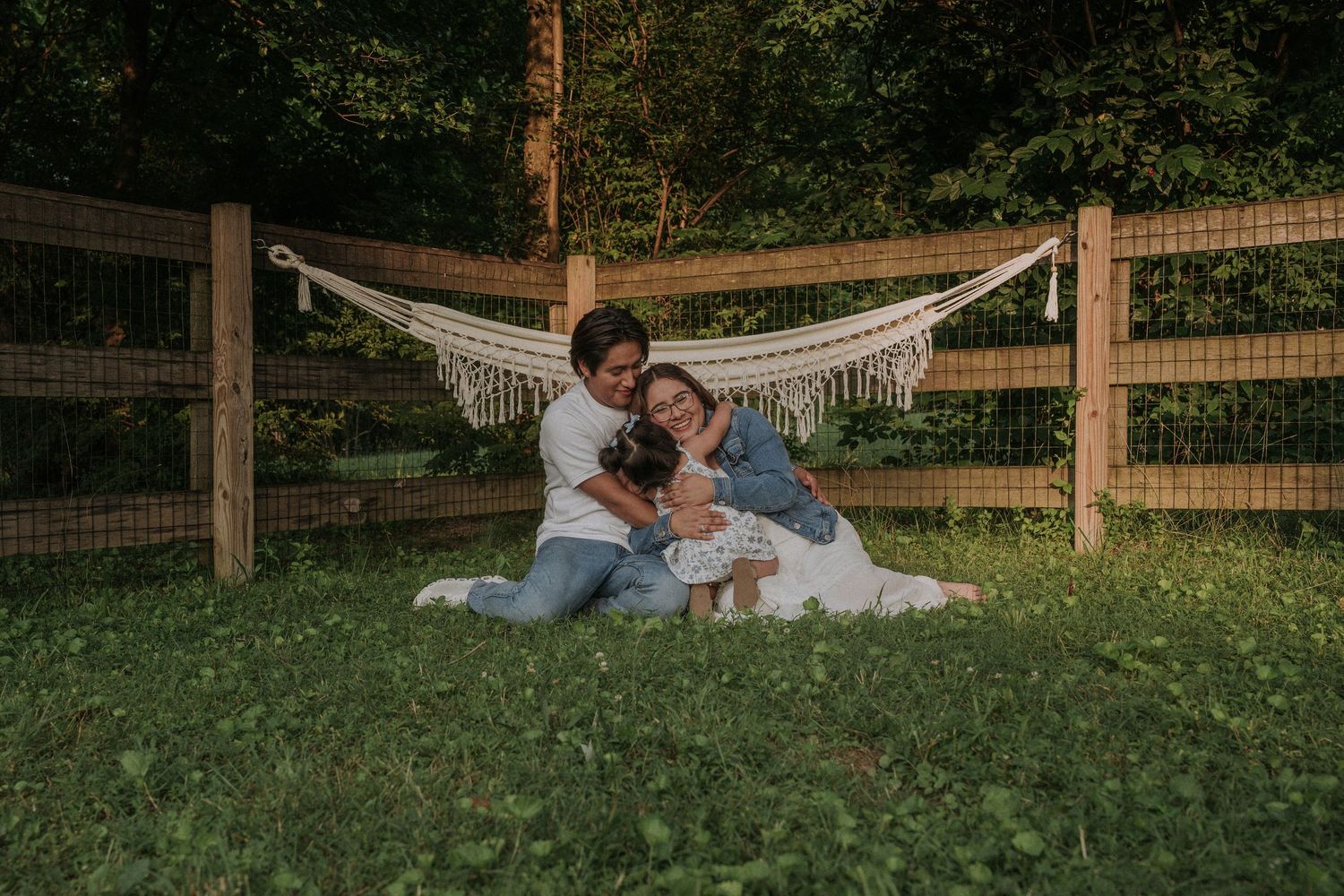 Couple relaxing on grass near a wooden fence at sunset.