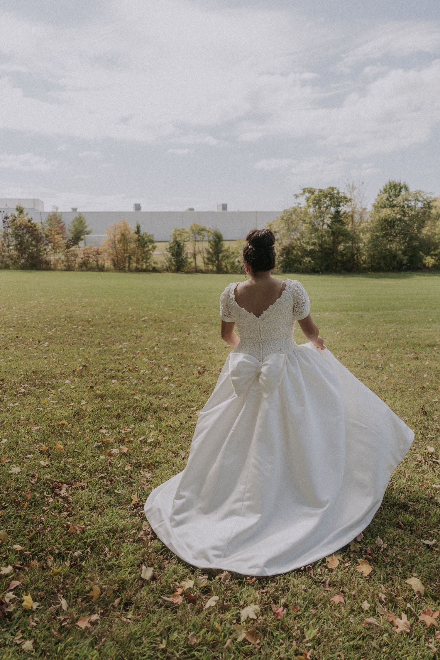 Bride in flowing white dress twirling in a sunny autumn field.