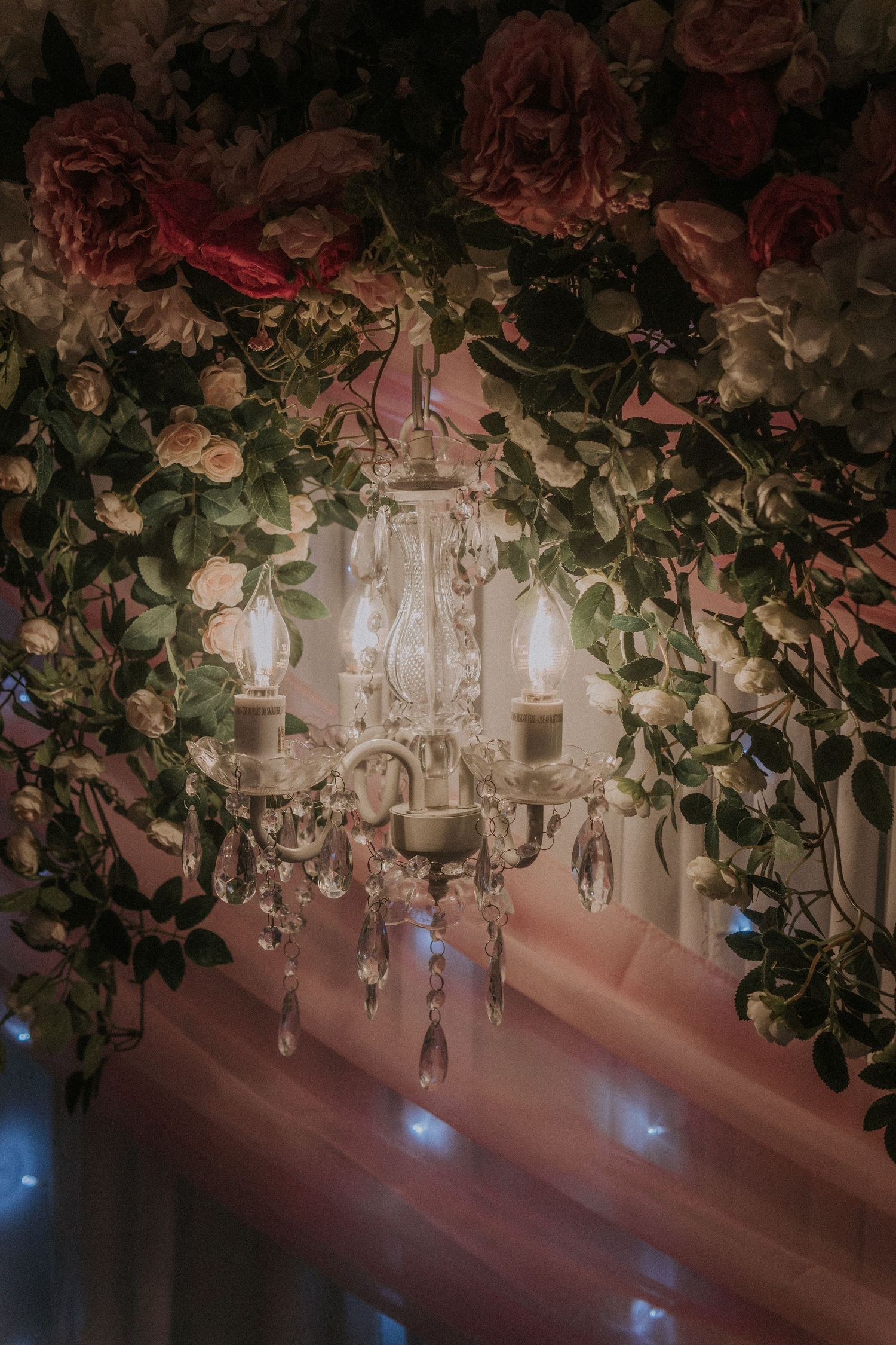 Crystal chandeliers and floral arrangements create a romantic ceiling display at an event venue.