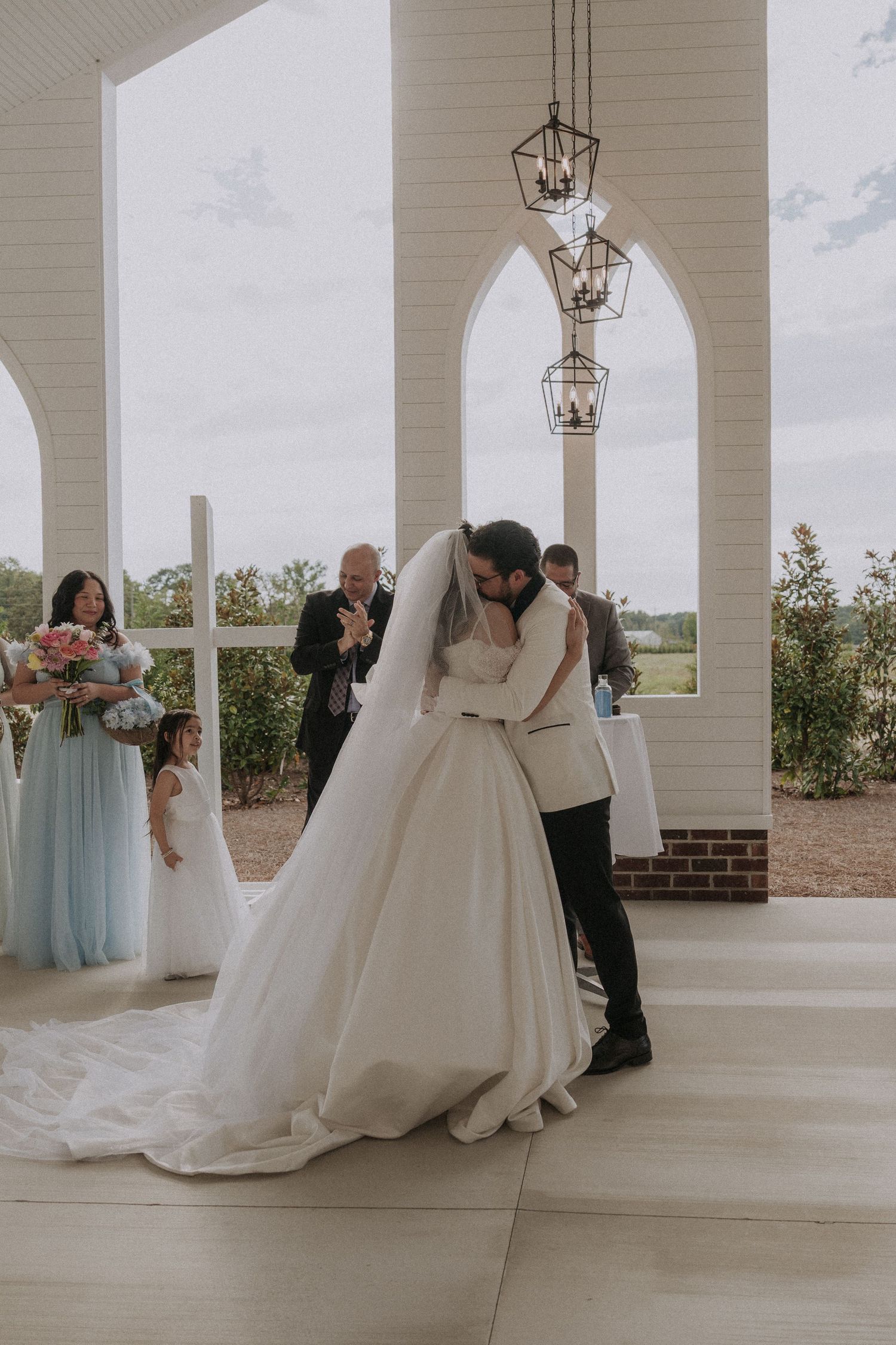 Bride and groom share first kiss at altar surrounded by bridesmaids in blue dresses.