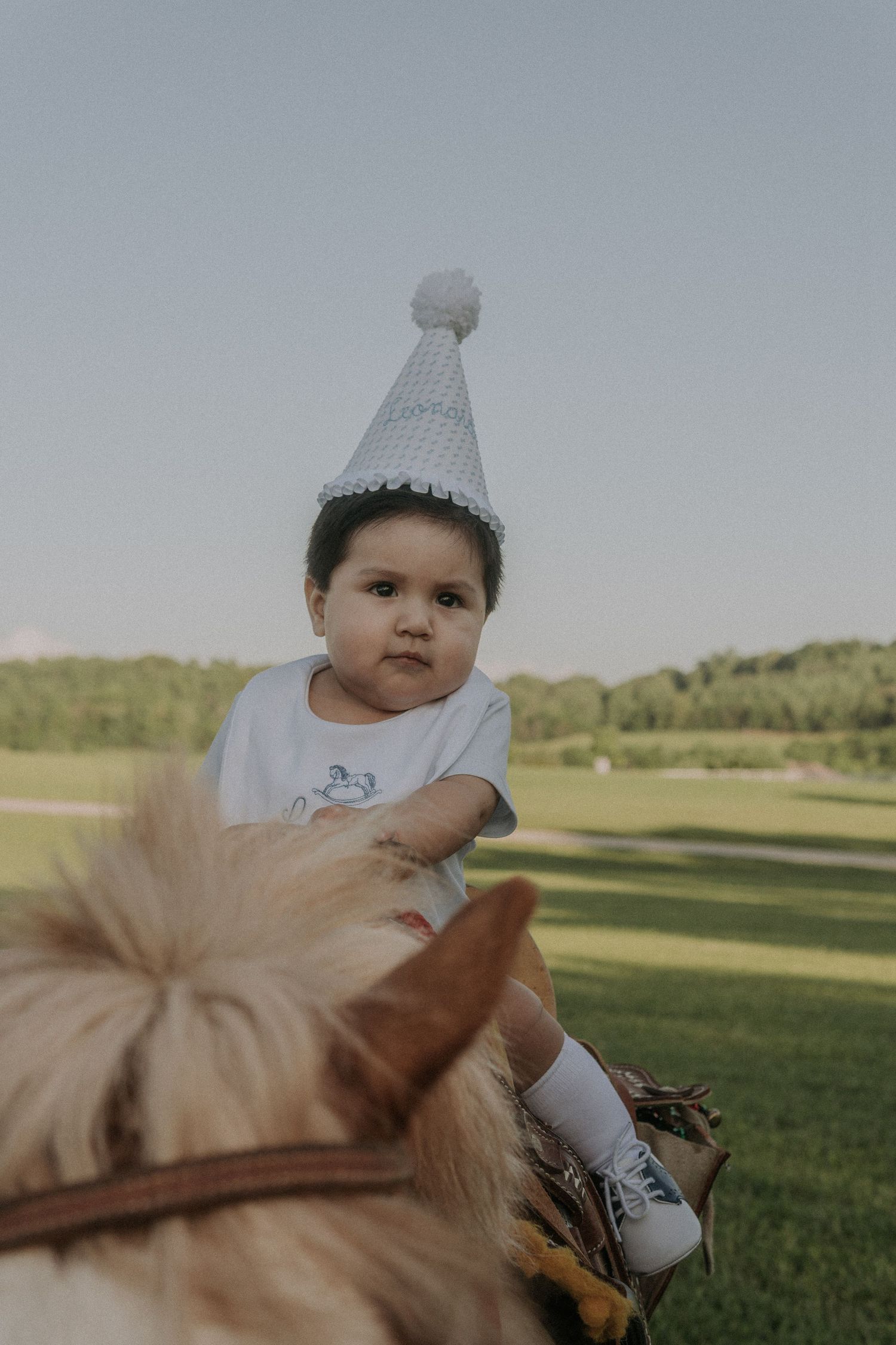 Child wearing celebration hat and white shirt in outdoor setting during golden hour.