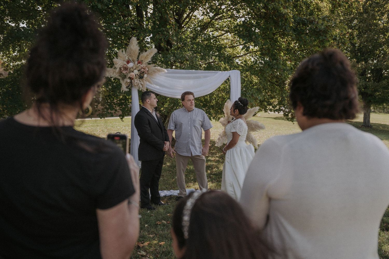 Wedding ceremony setup in an outdoor garden with white fabric draping and floral decorations.