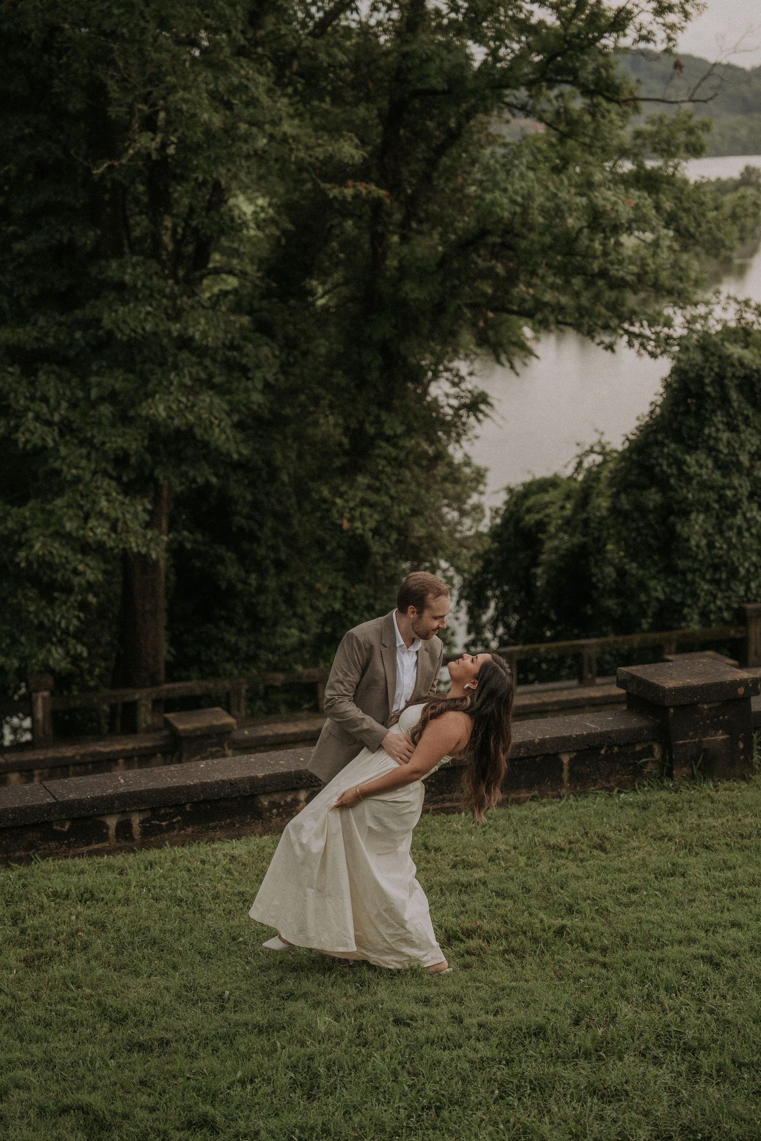 Romantic engagement photos on a grassy hillside with stone railing and natural scenery.